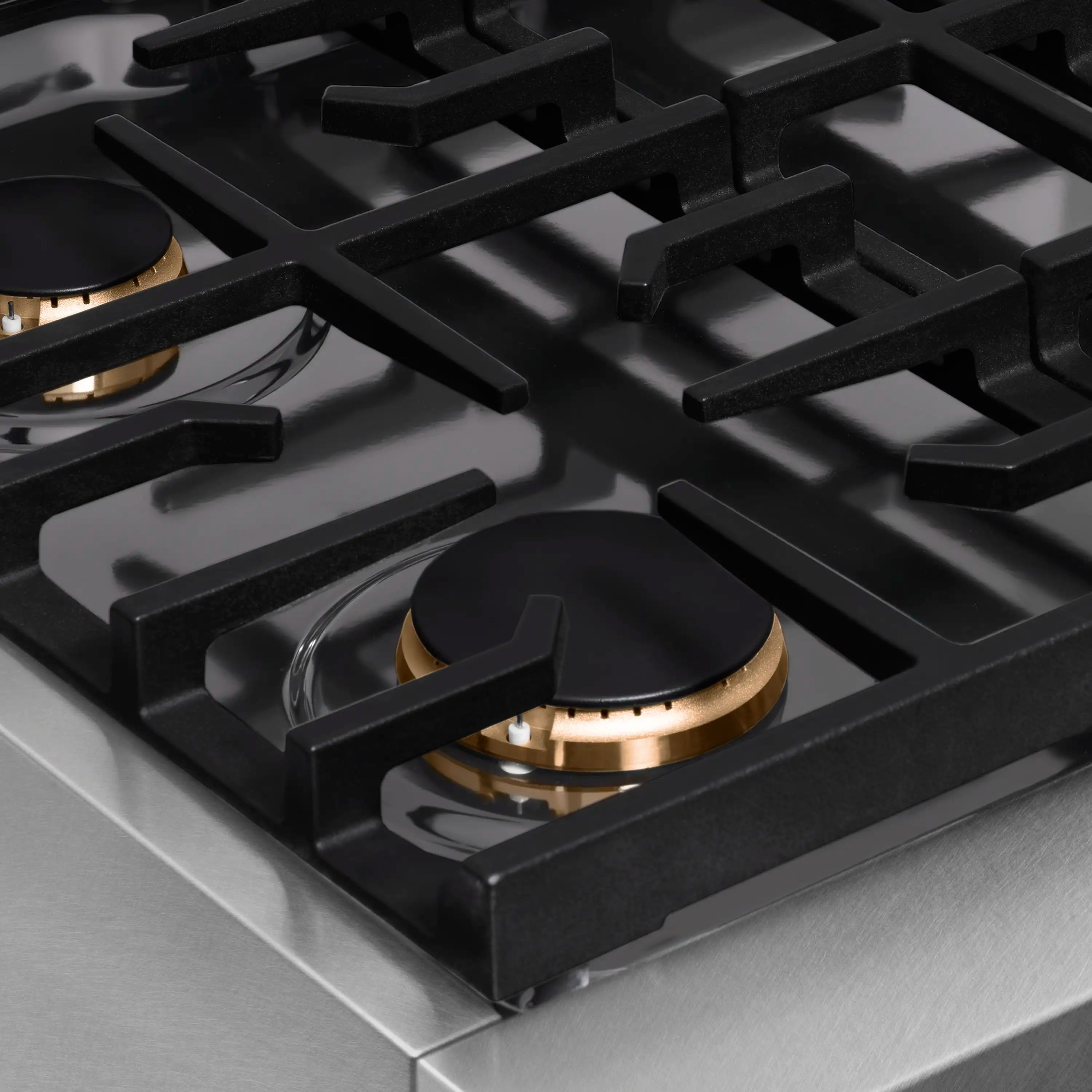 Close-up of a brass-trim gas burner with black grate on a satin stainless steel surface