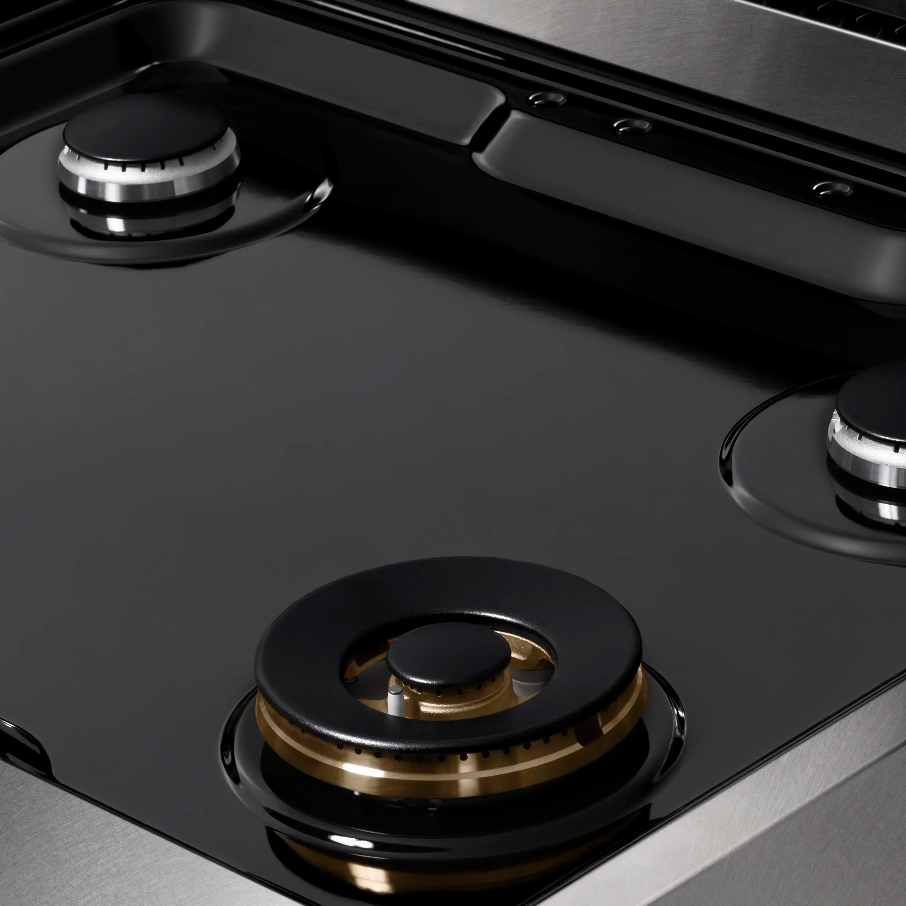 Gas rangetop burner with black cap and brass-toned base on satin stainless steel