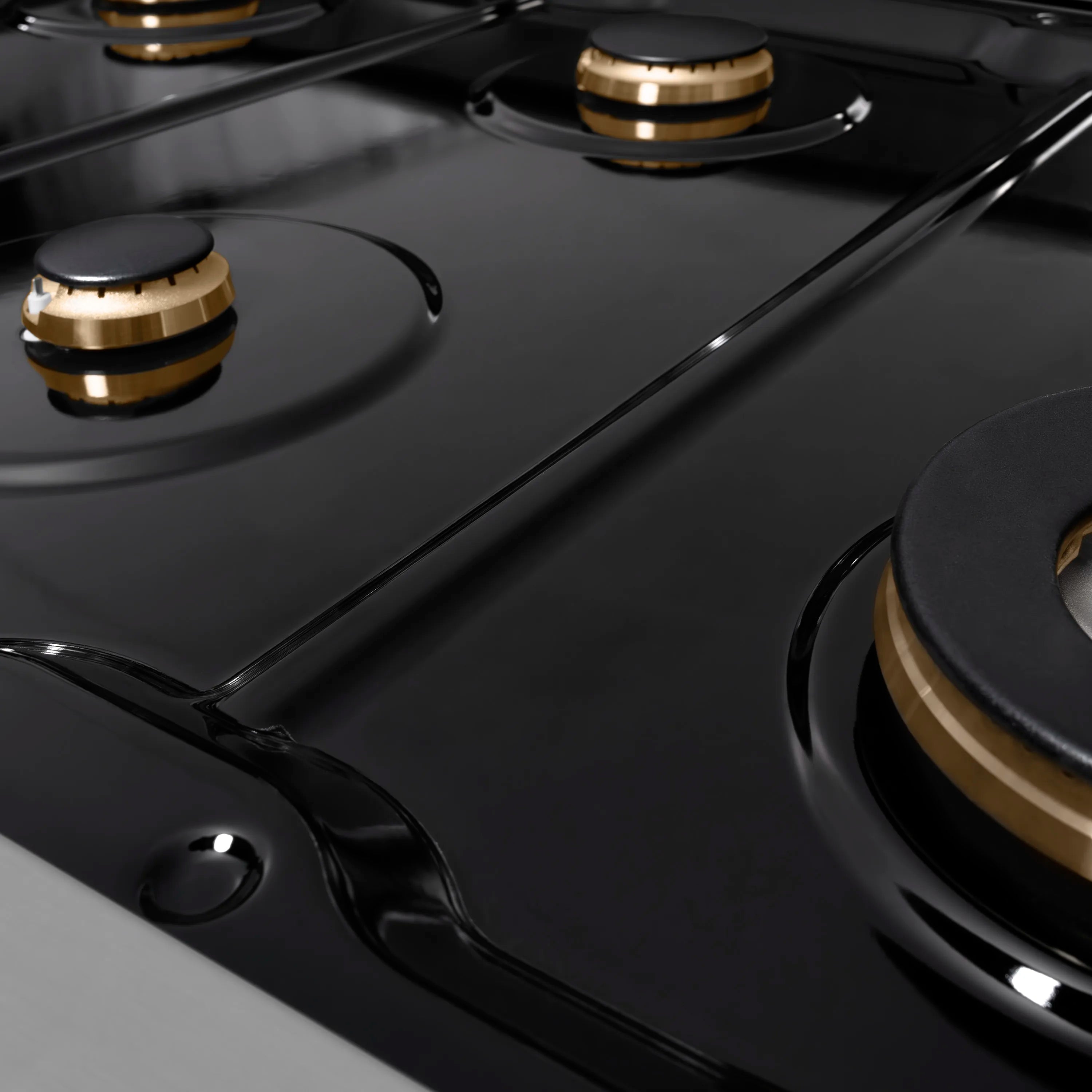 Stainless cooktop surface with black burner grates and champagne-bronze burner rings