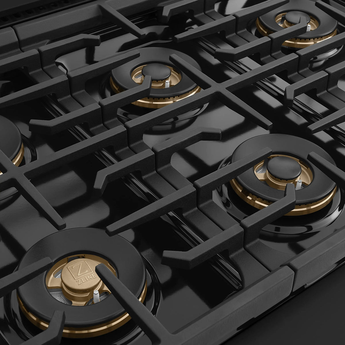 Black gas cooktop with several burners, cast grates, and champagne bronze accents