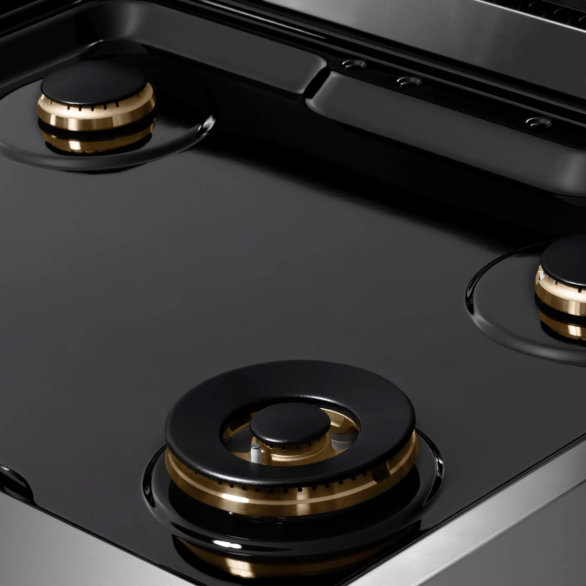 Gas rangetop burner with black cap and gold ring detail on glossy surface