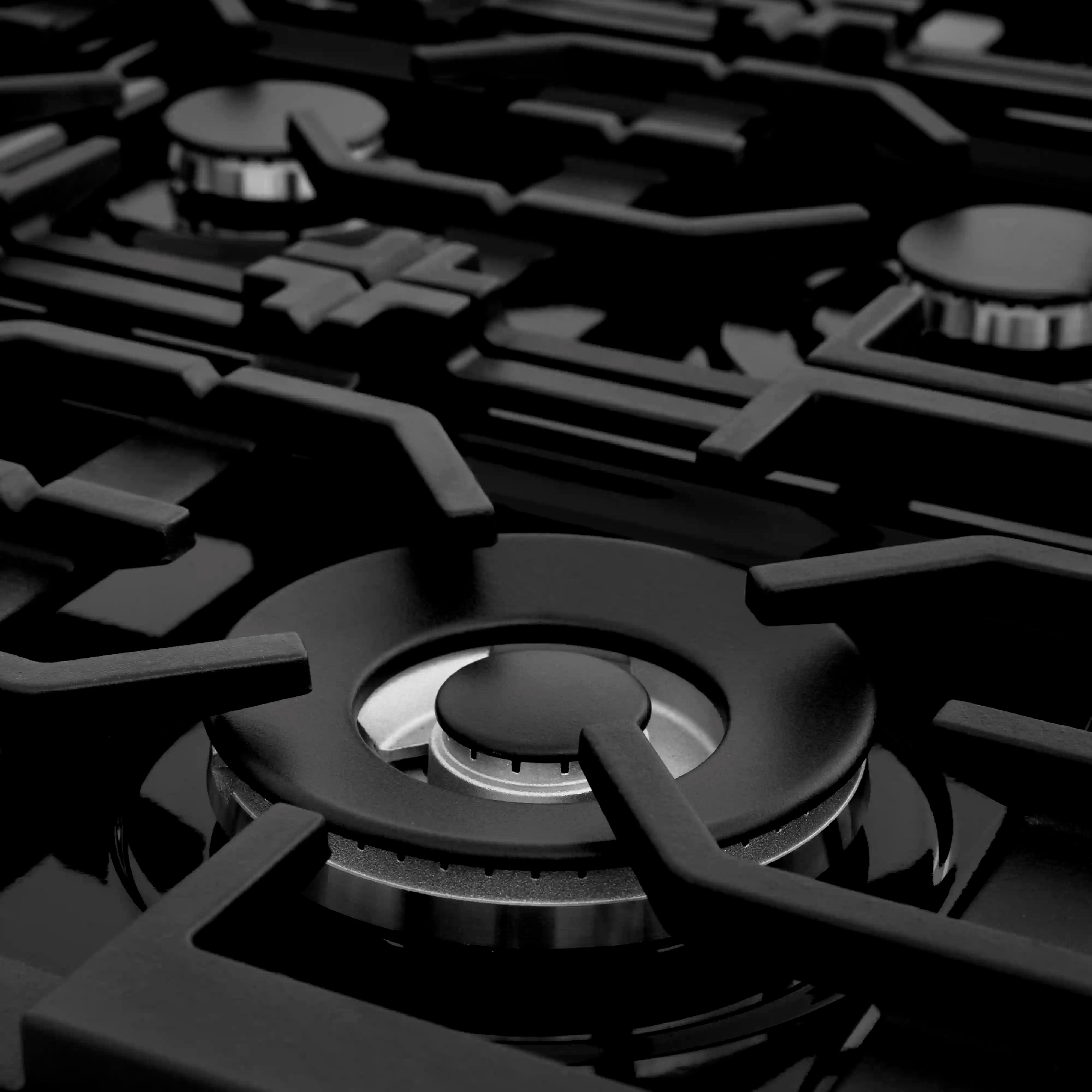 Close-up of a black gas burner with cast-iron grate on a stainless steel rangetop