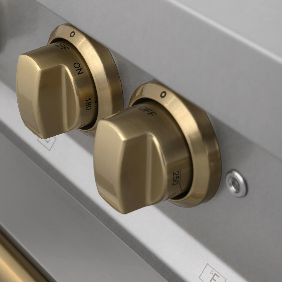 Close-up of champagne bronze dual control knobs on a stainless range panel