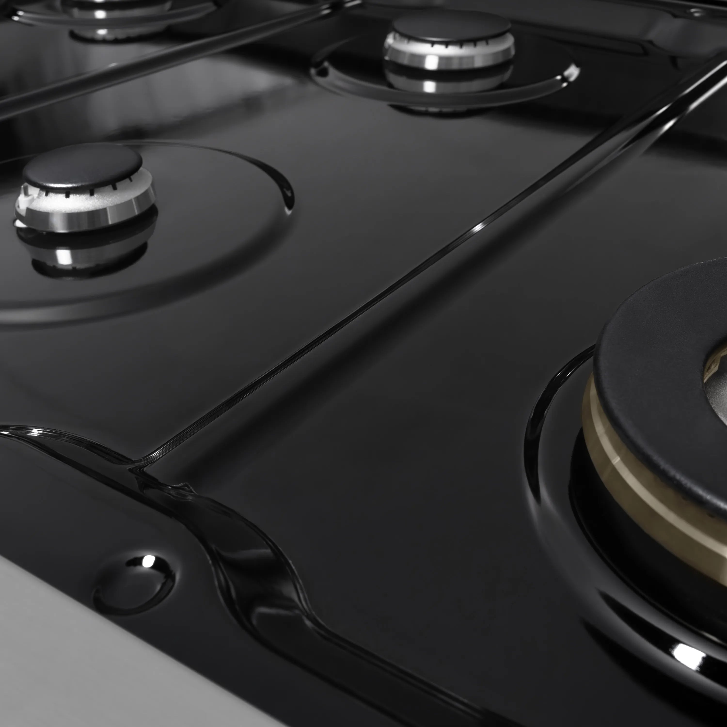 Close-up of a stainless gas cooktop with black burner grates and control caps
