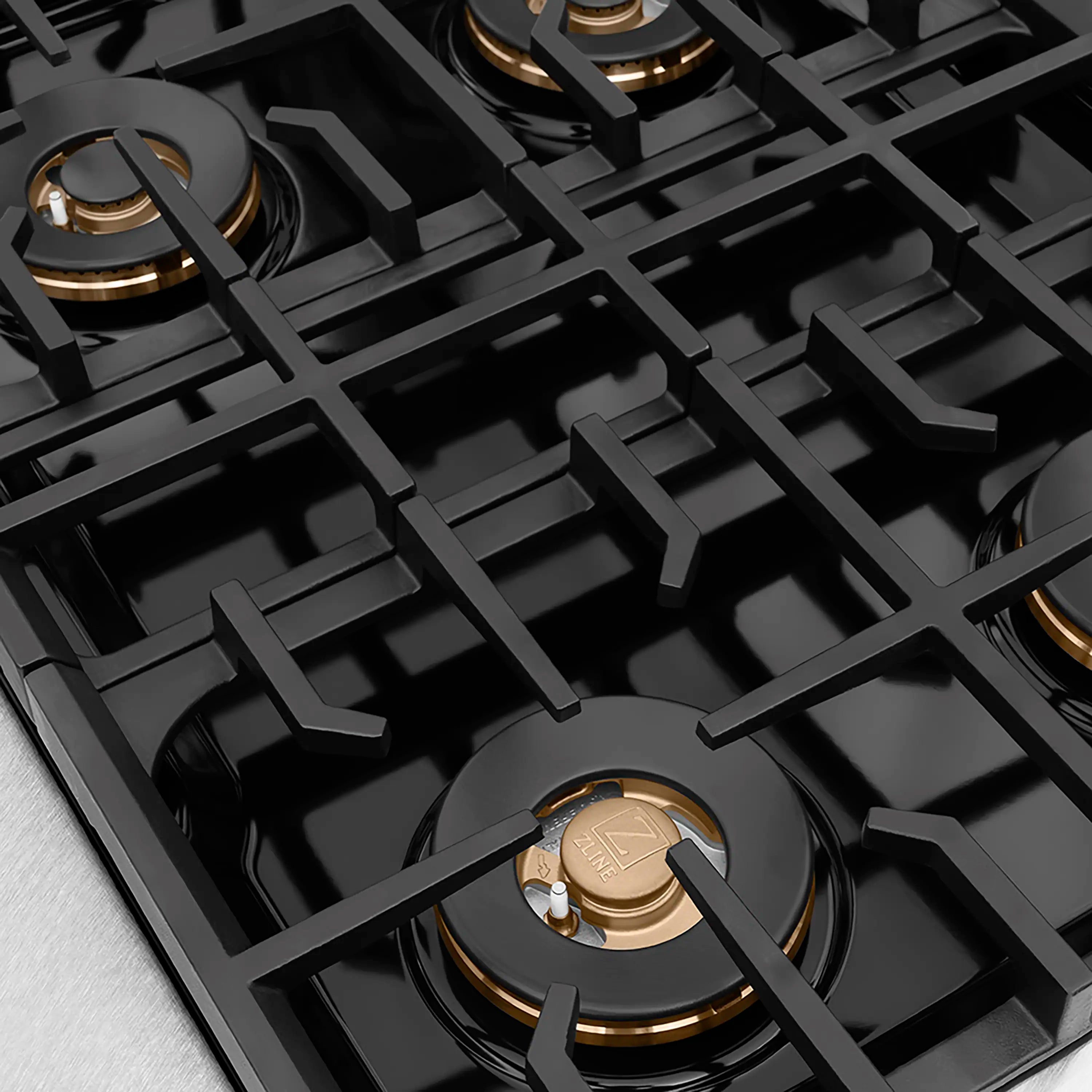 Gas cooktop grate with burner caps and bronze accents on black enamel supports