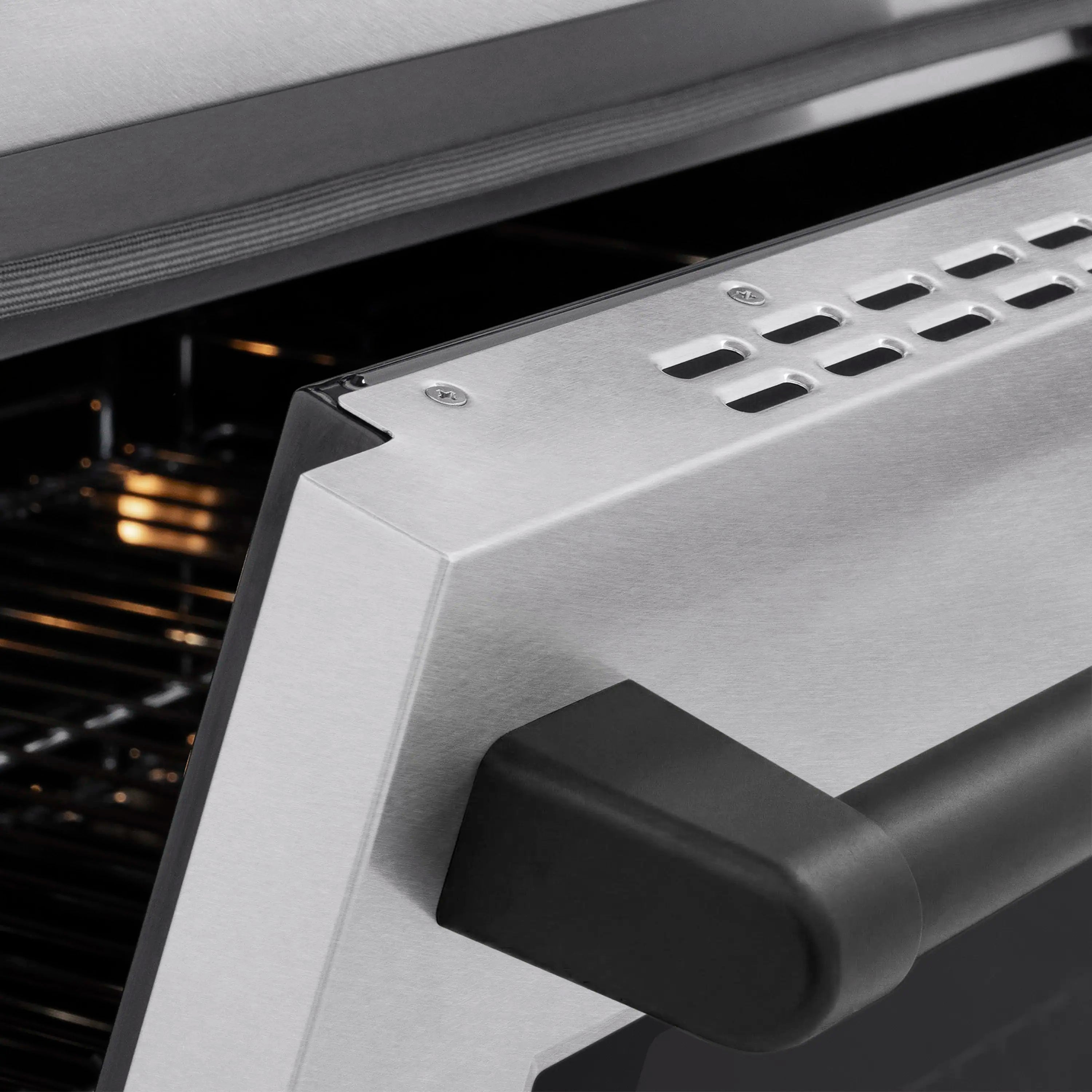 Stainless steel oven door corner with matte black handle and ventilation grille