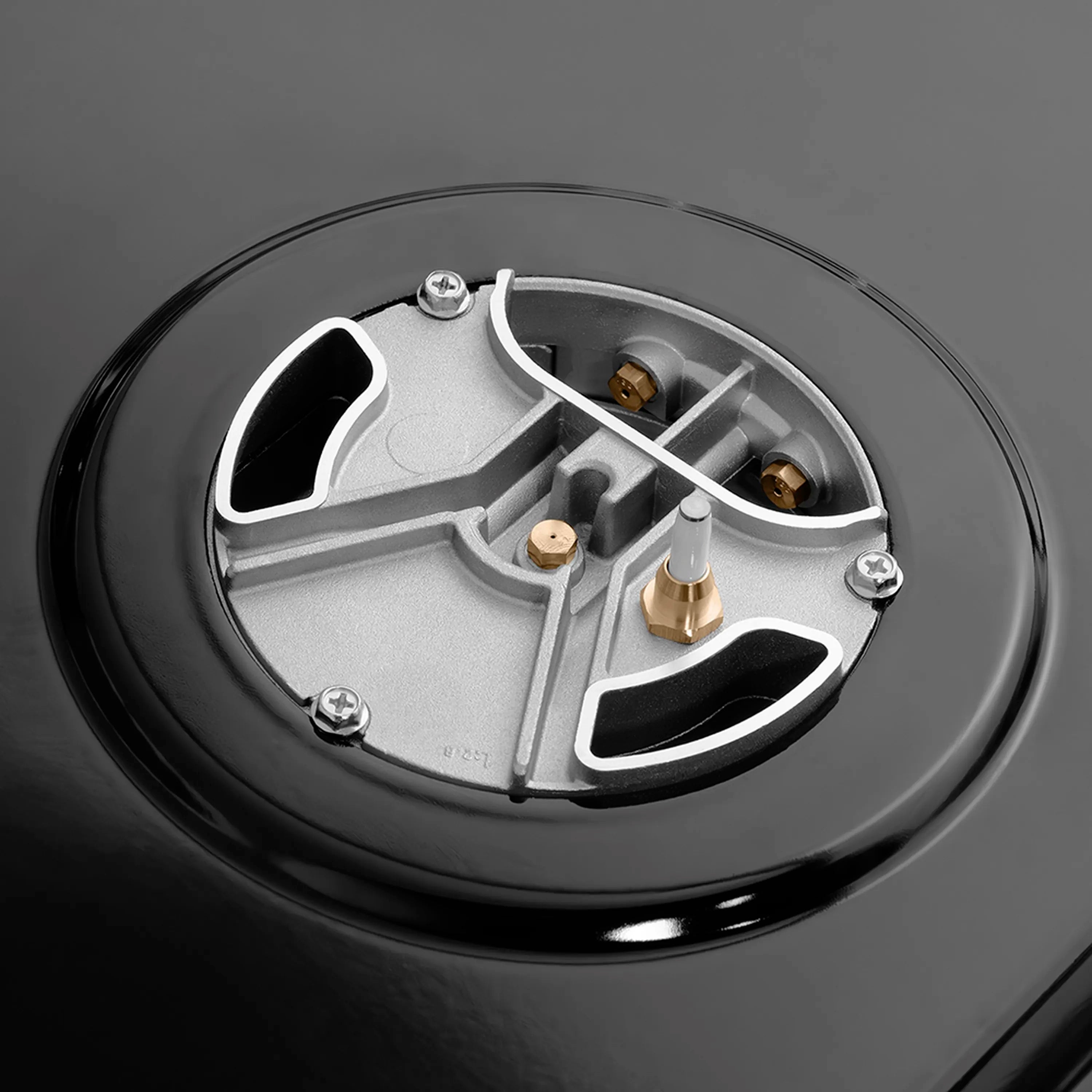 Round gas burner head with brass ports and black burner cap on stovetop