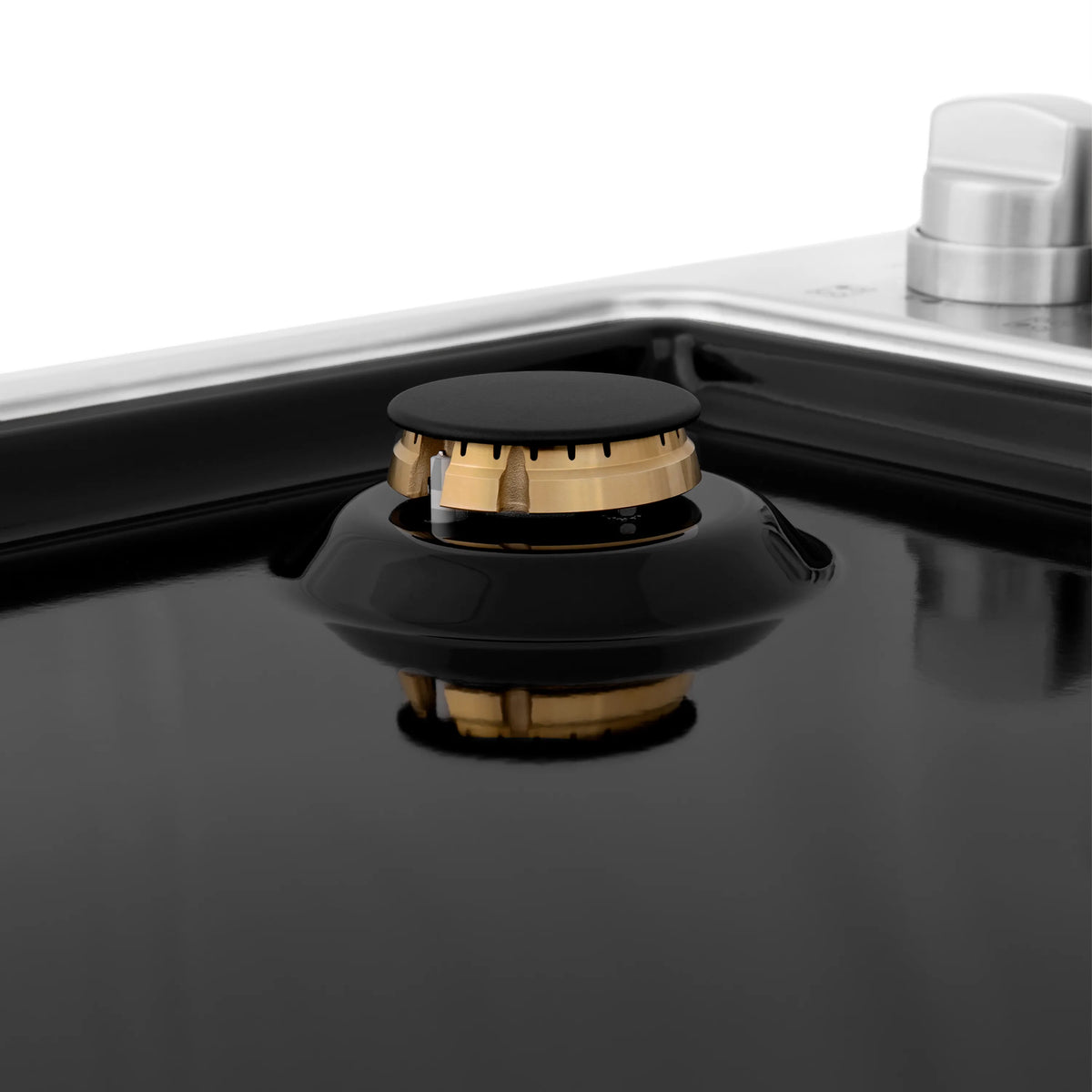 Black gas cooktop burner with brass flame ring and black cap, viewed from above