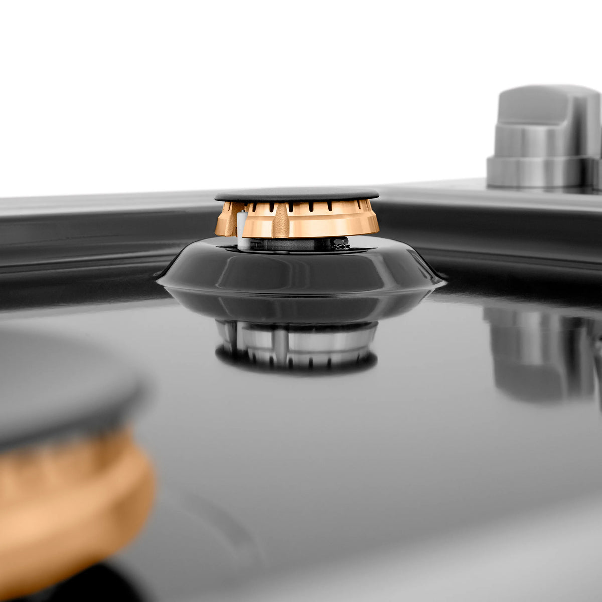 Black gas burner with brass cap on glossy black porcelain top, angled view