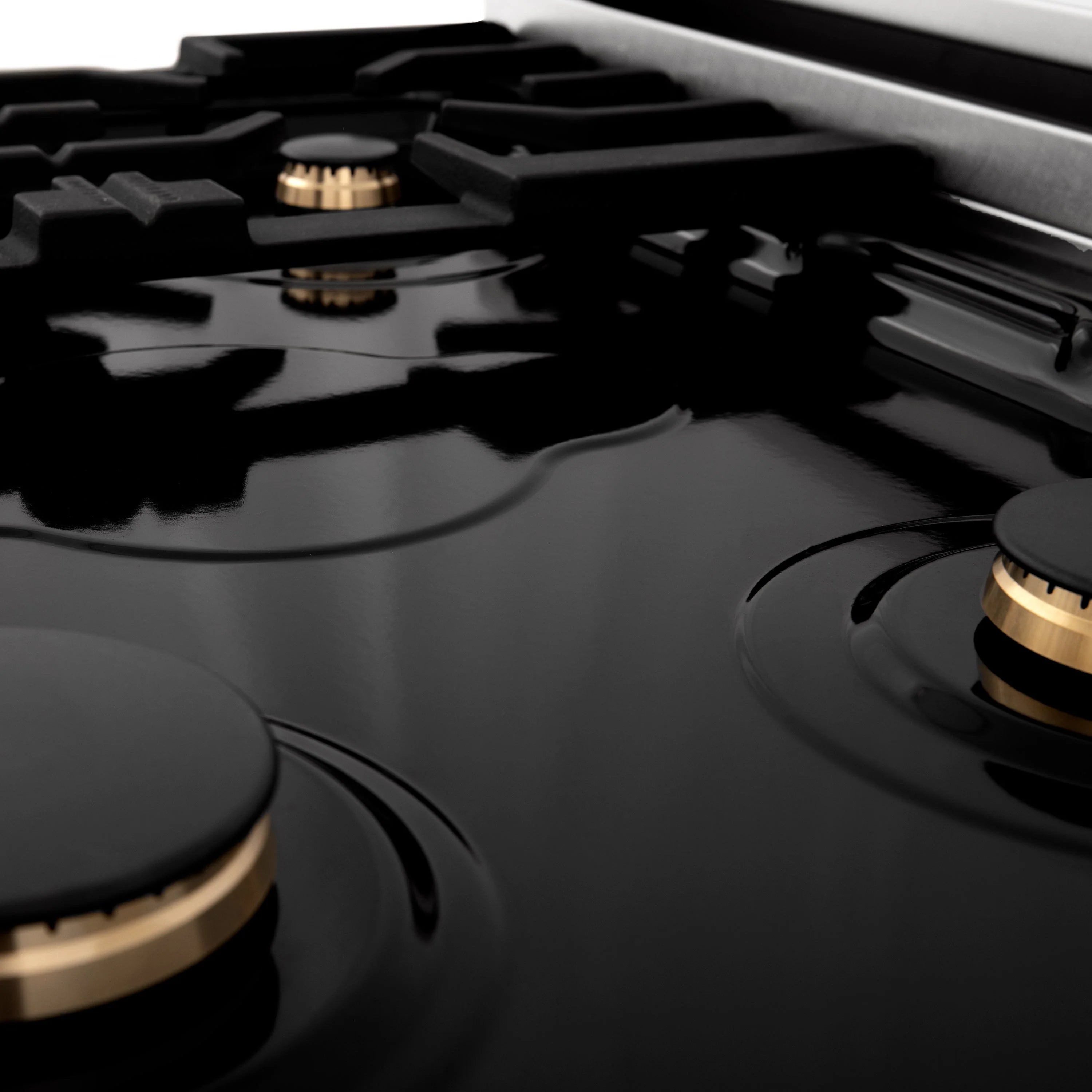 Top view of black gas burners with brass caps on a dark griddle-ready cooktop