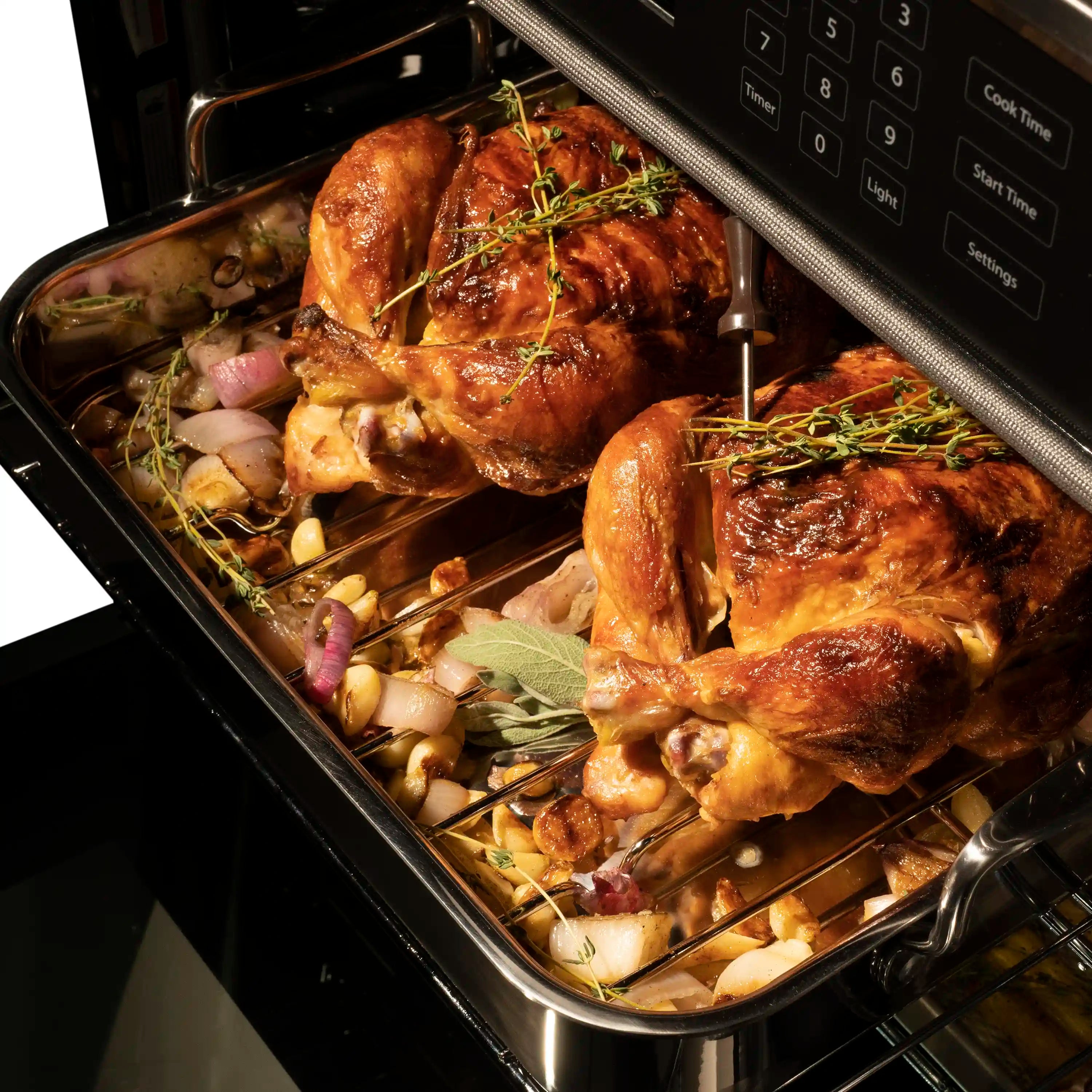 Stainless steel oven interior with roasted chicken on a tray with herbs