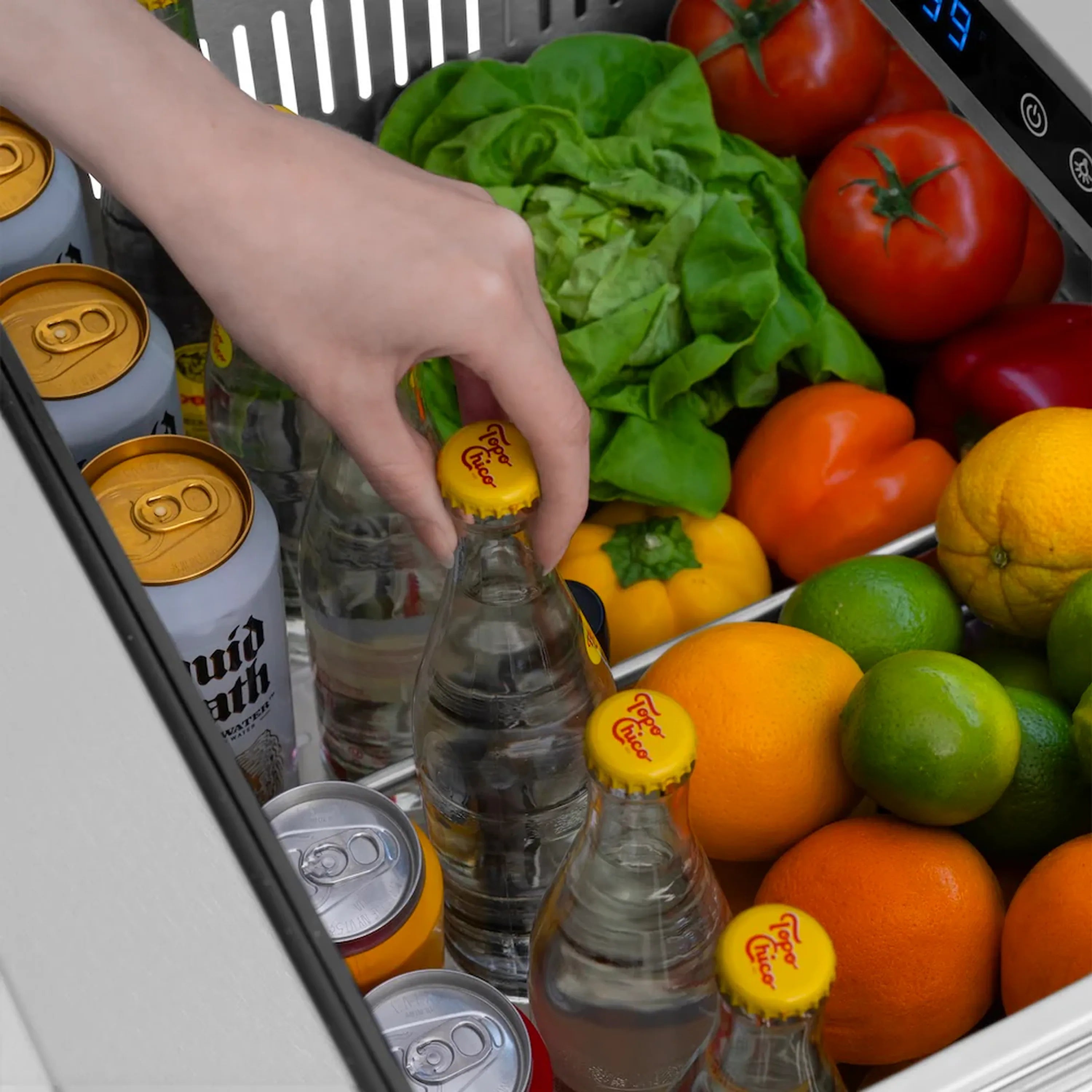 Refrigerator drawer interior with hand arranging bottled drinks among fresh vegetables and fruit