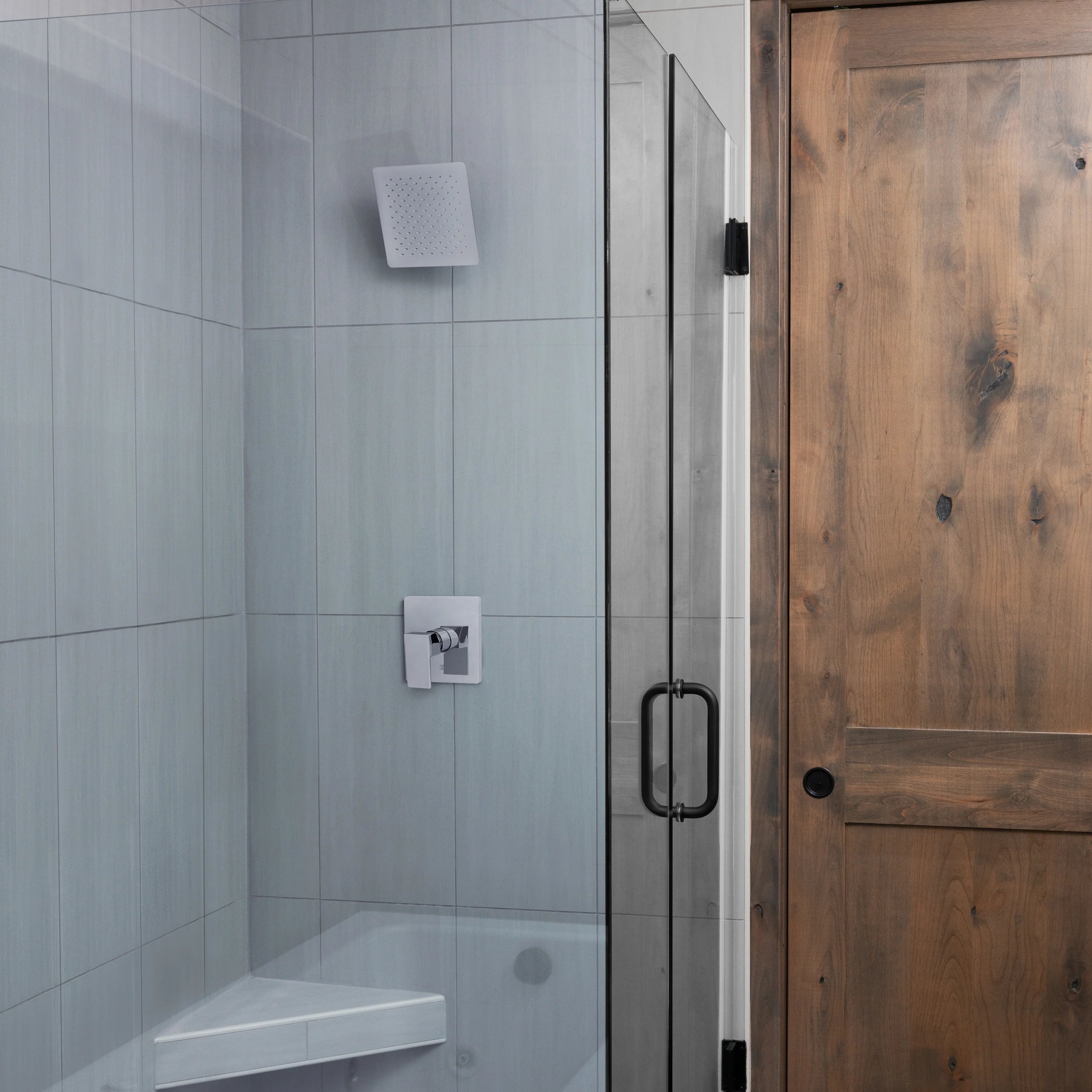 Oversized square chrome shower head mounted in a shower wall, fixed spray face