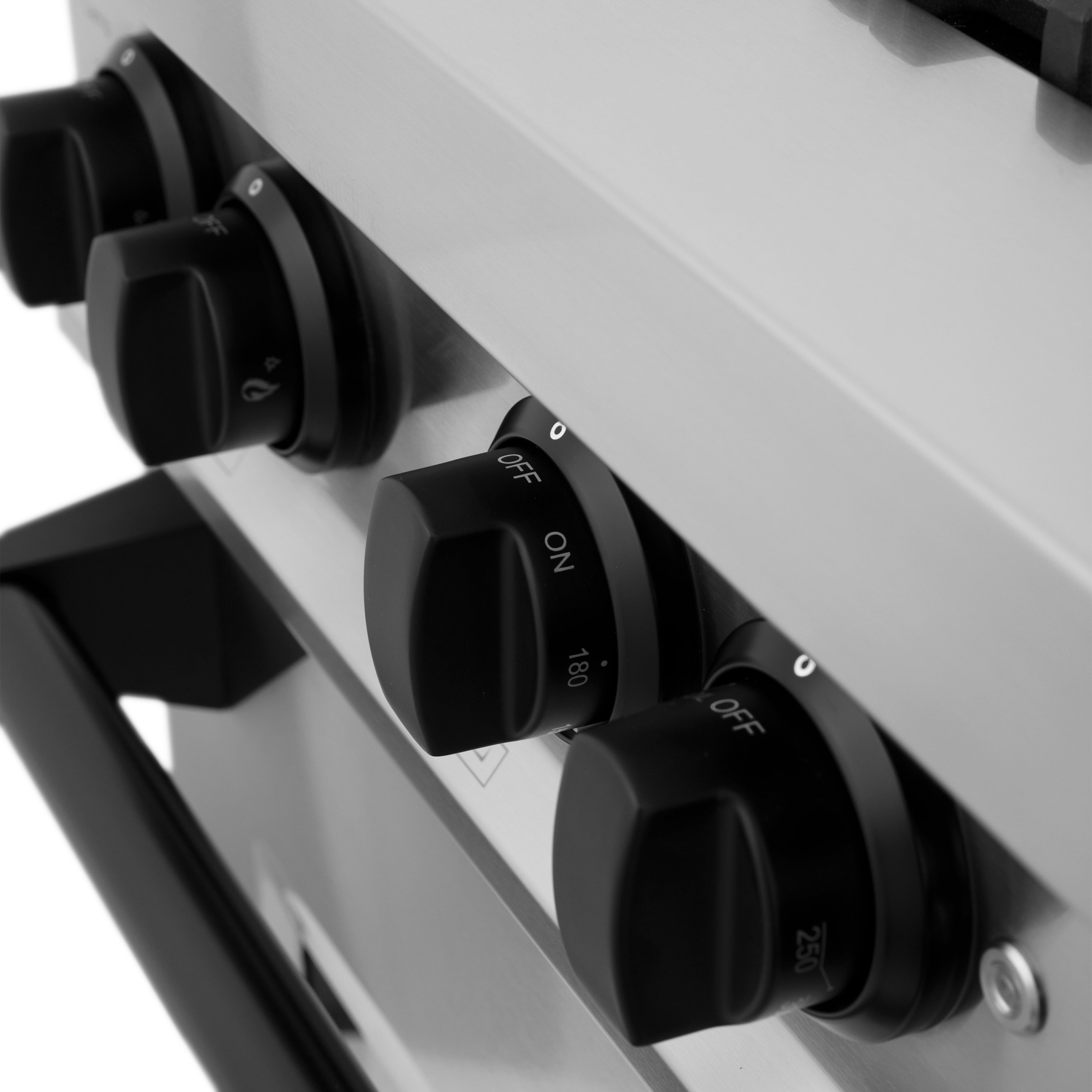 Close-up of matte black range control knobs with off markings on stainless panel