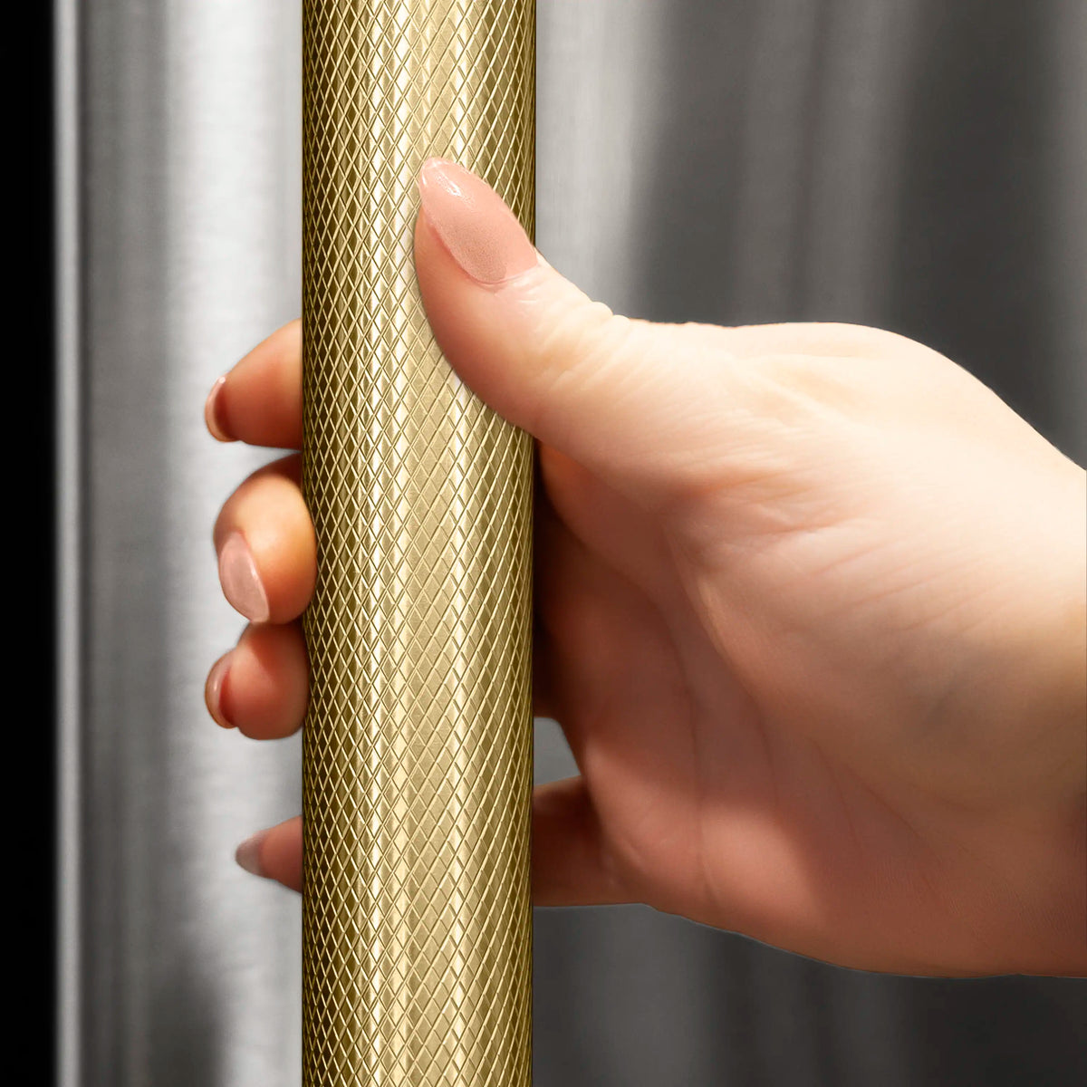 Hand touching bronze helix handle on a stainless beverage refrigerator