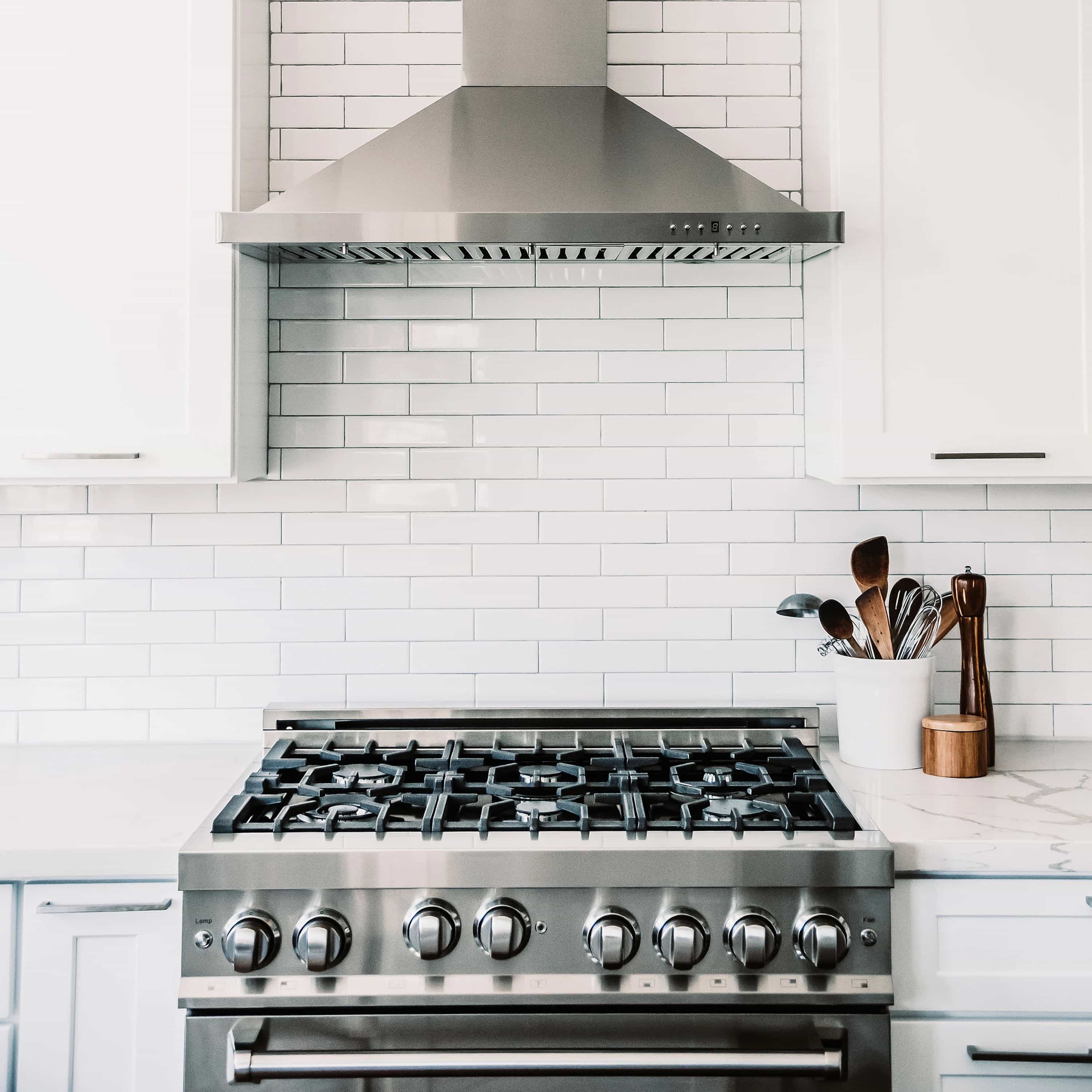 Stainless steel gas range with burners and convertible hood above a tile backsplash