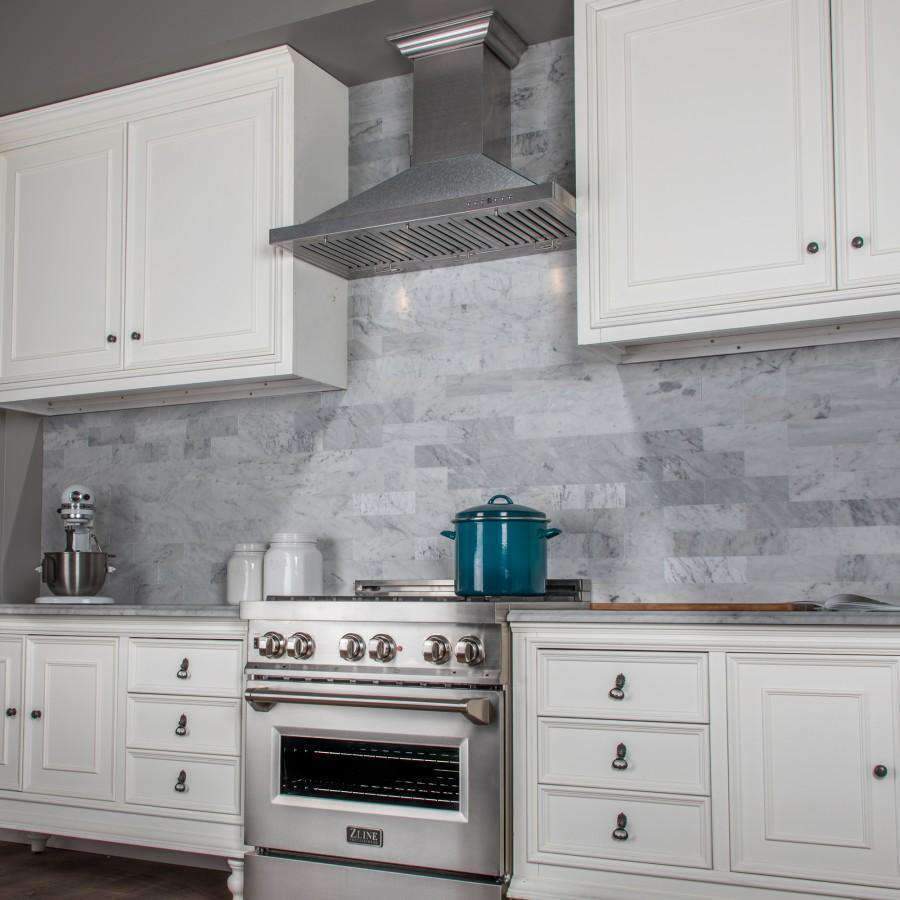 Satin stainless steel range hood above built-in gas range with knobs and oven door