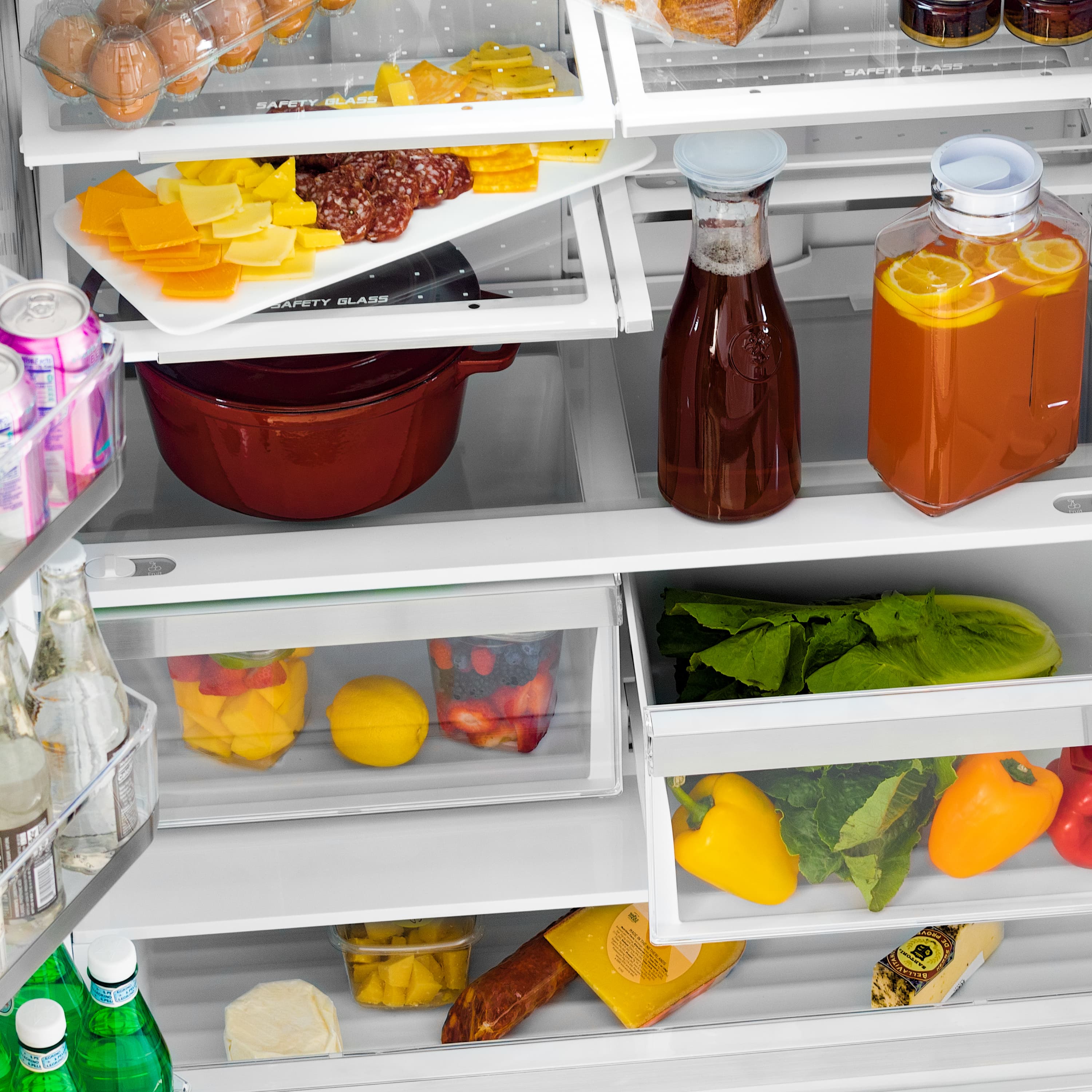 Refrigerator shelves with containers of fruit, vegetables, cheese, and drink bottles
