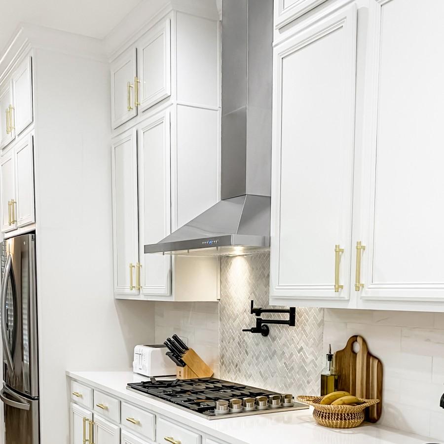 Stainless steel wall range hood above gas cooktop with white cabinetry