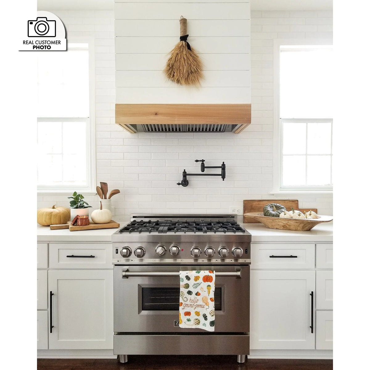 Stainless steel range hood insert under cabinet above a gas stove in a bright kitchen