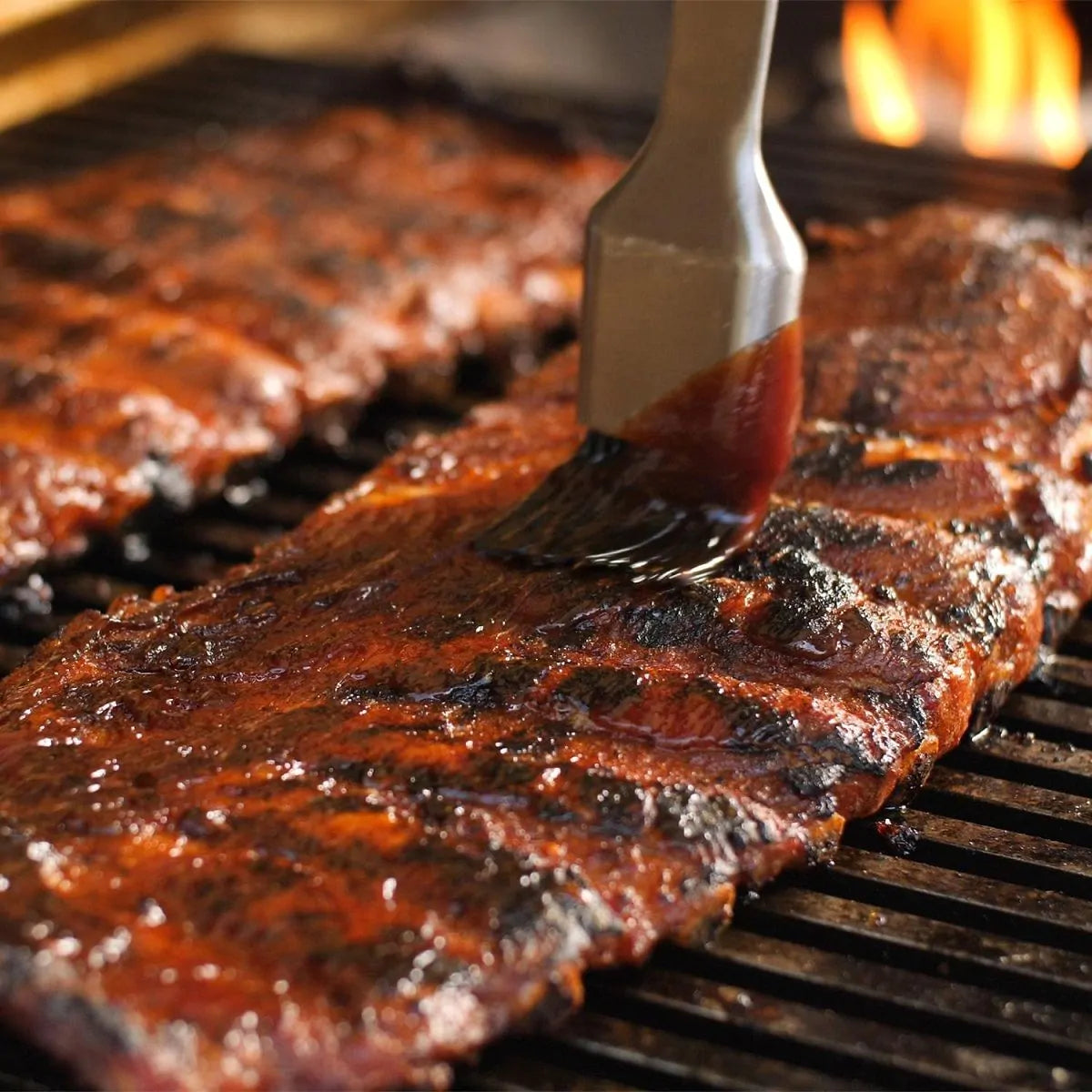 Gas grill grates with seared meat and visible flames