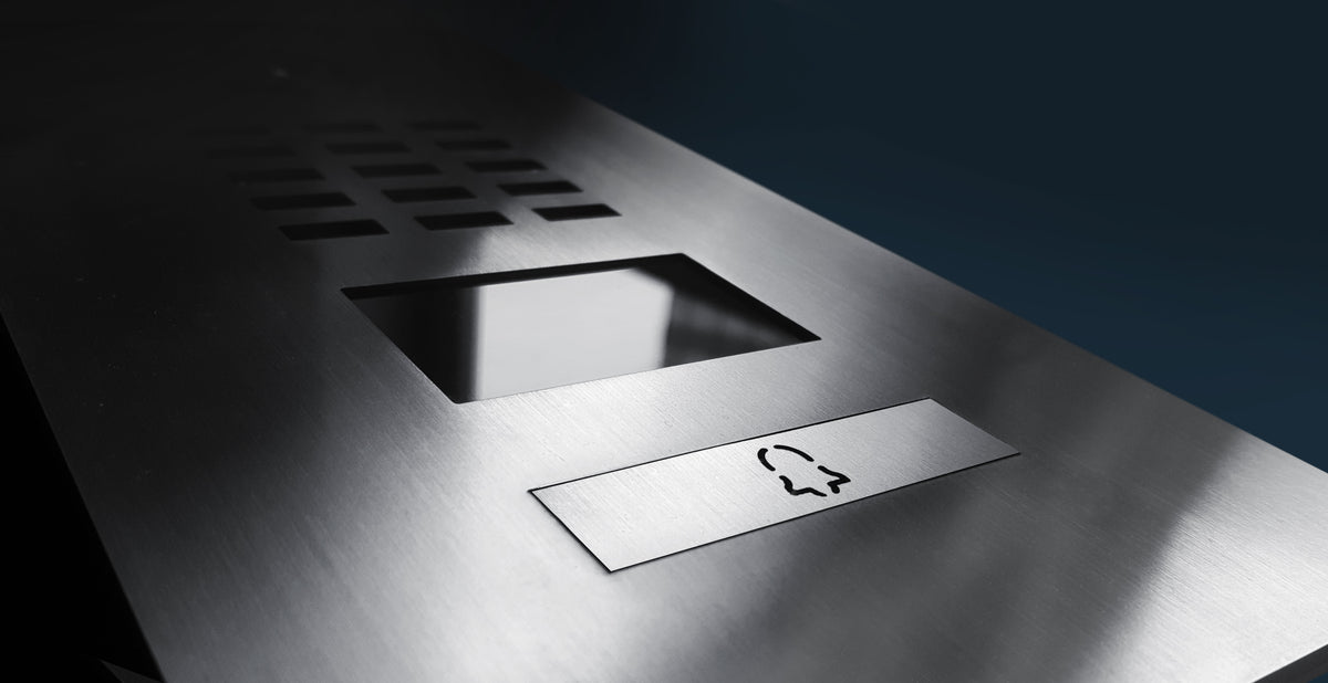 Close-up of brushed metal video door station panel with speaker and label slot.