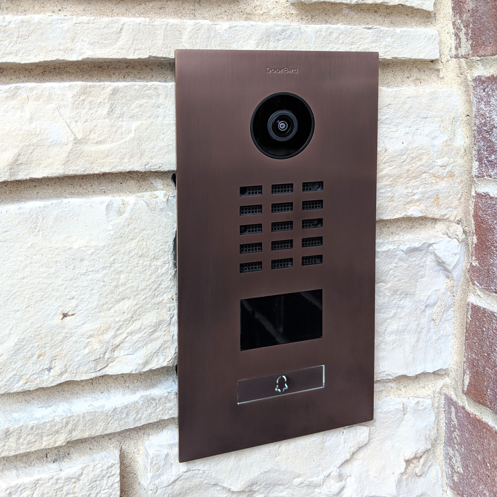 Bronze DoorBird video door station with camera lens, keypad panel, and screen; label