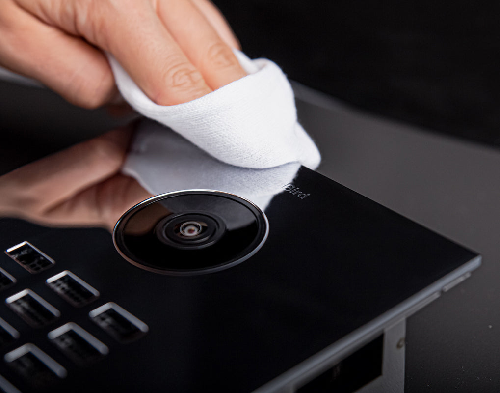 Chrome video door camera on door station, with hand wiping the lens