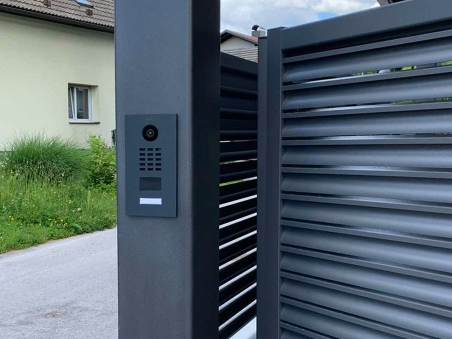 Titanium video door station call panel on wall beside metal gate
