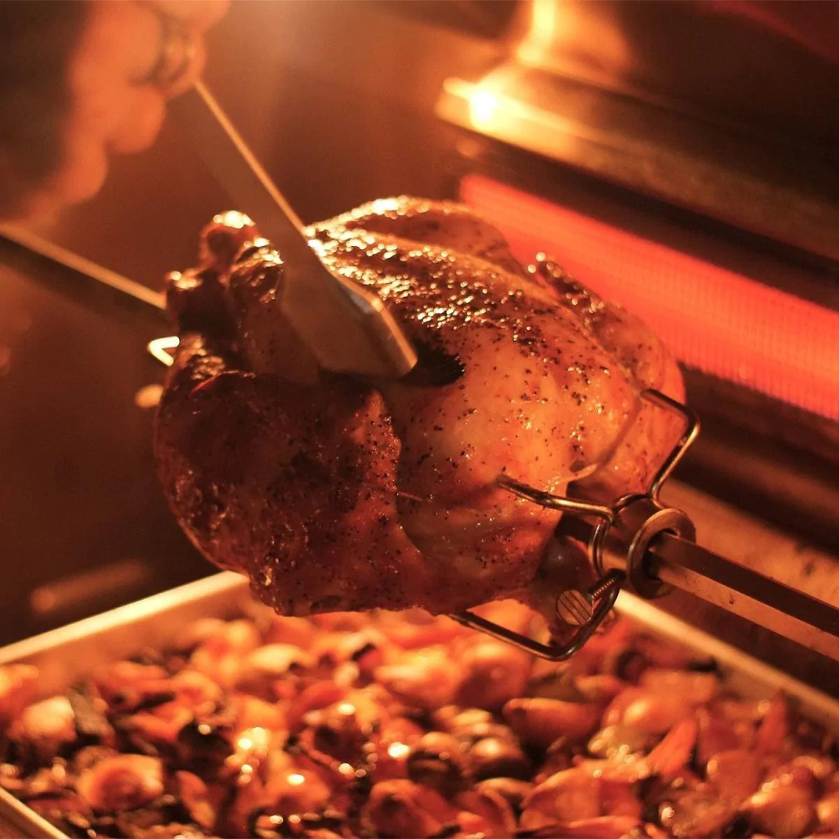 Rotisserie chicken roasting on grill spit above flame and glowing burner