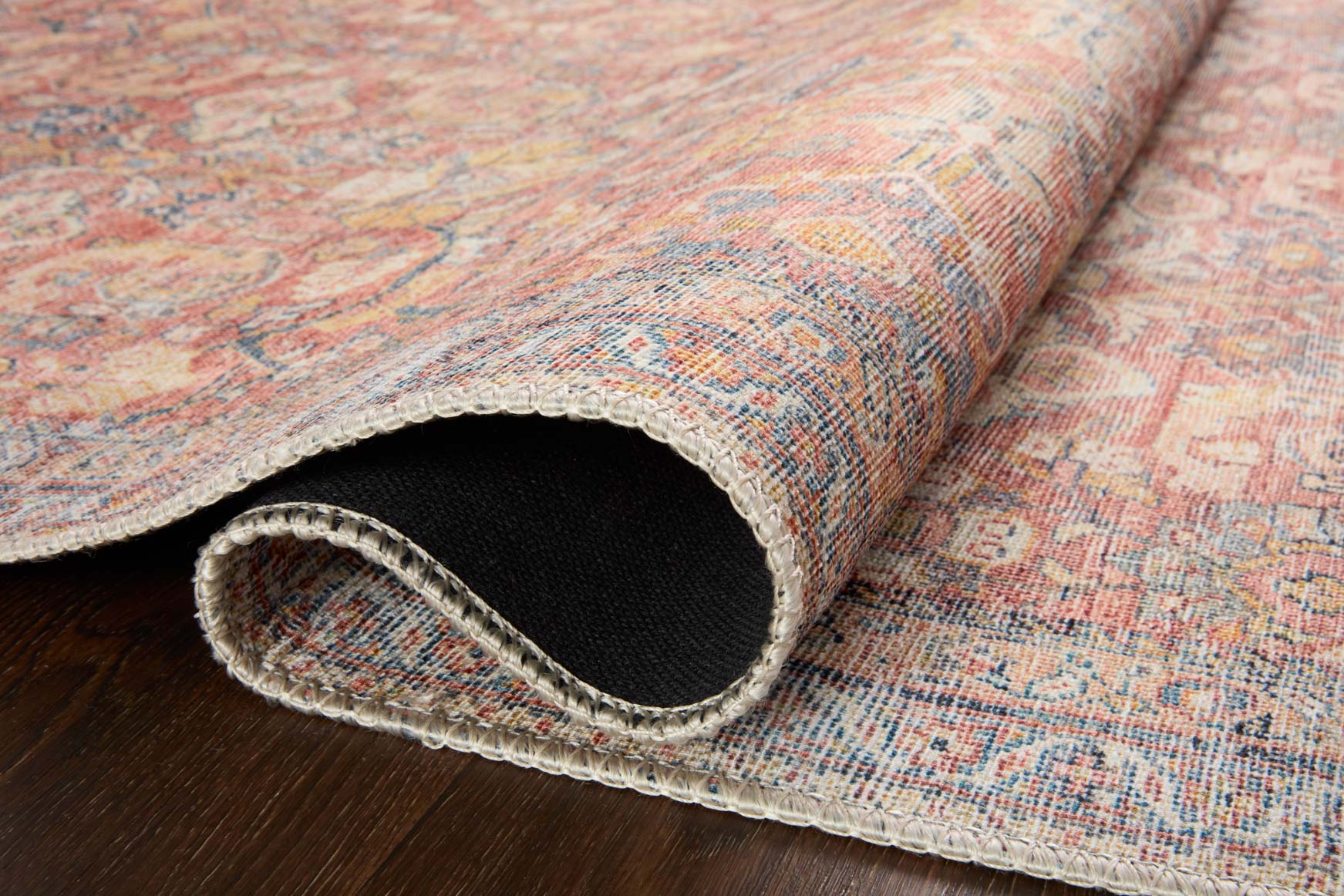 Traditional rug detail showing woven edge and dark backing; rust and denim blue.