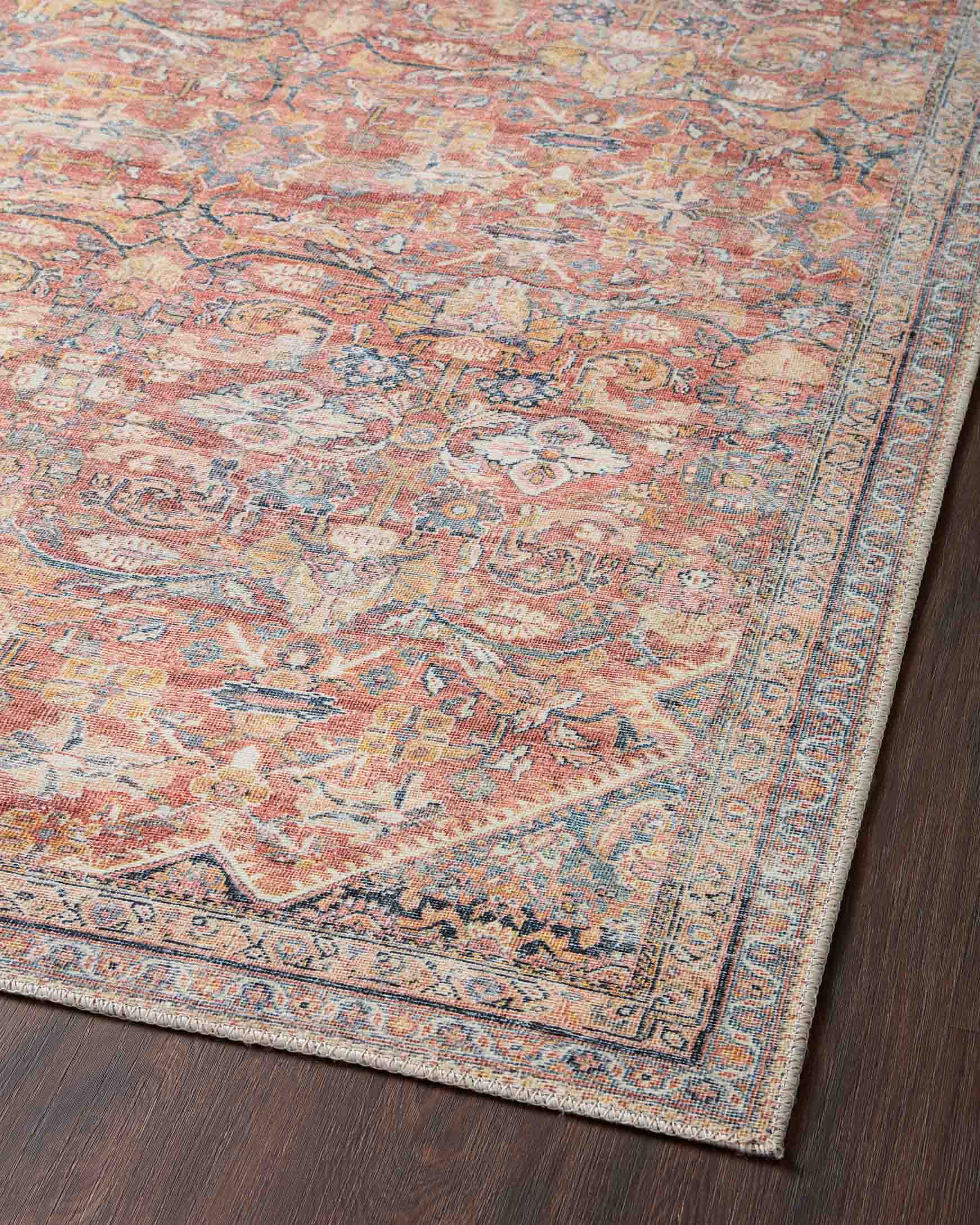 Traditional power-loomed rug close-up of patterned field and border in rust and denim.
