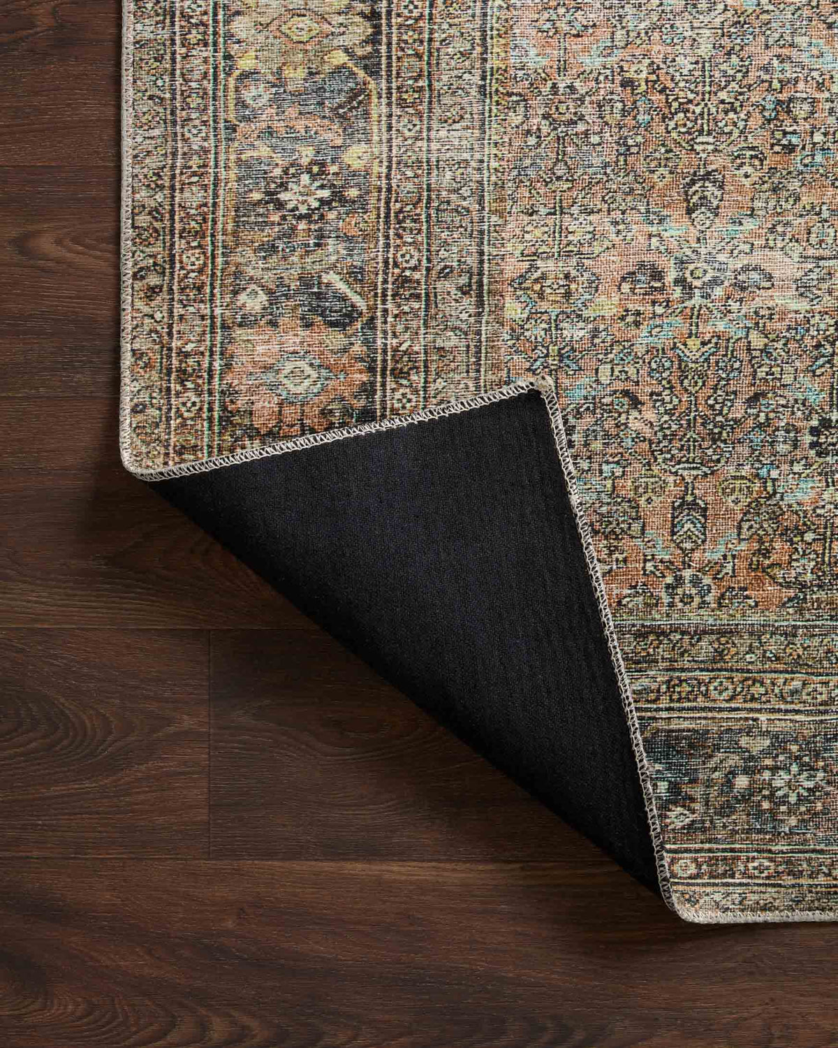 Rug corner close-up with rolled edge on dark wood floor, multicolor ornate border