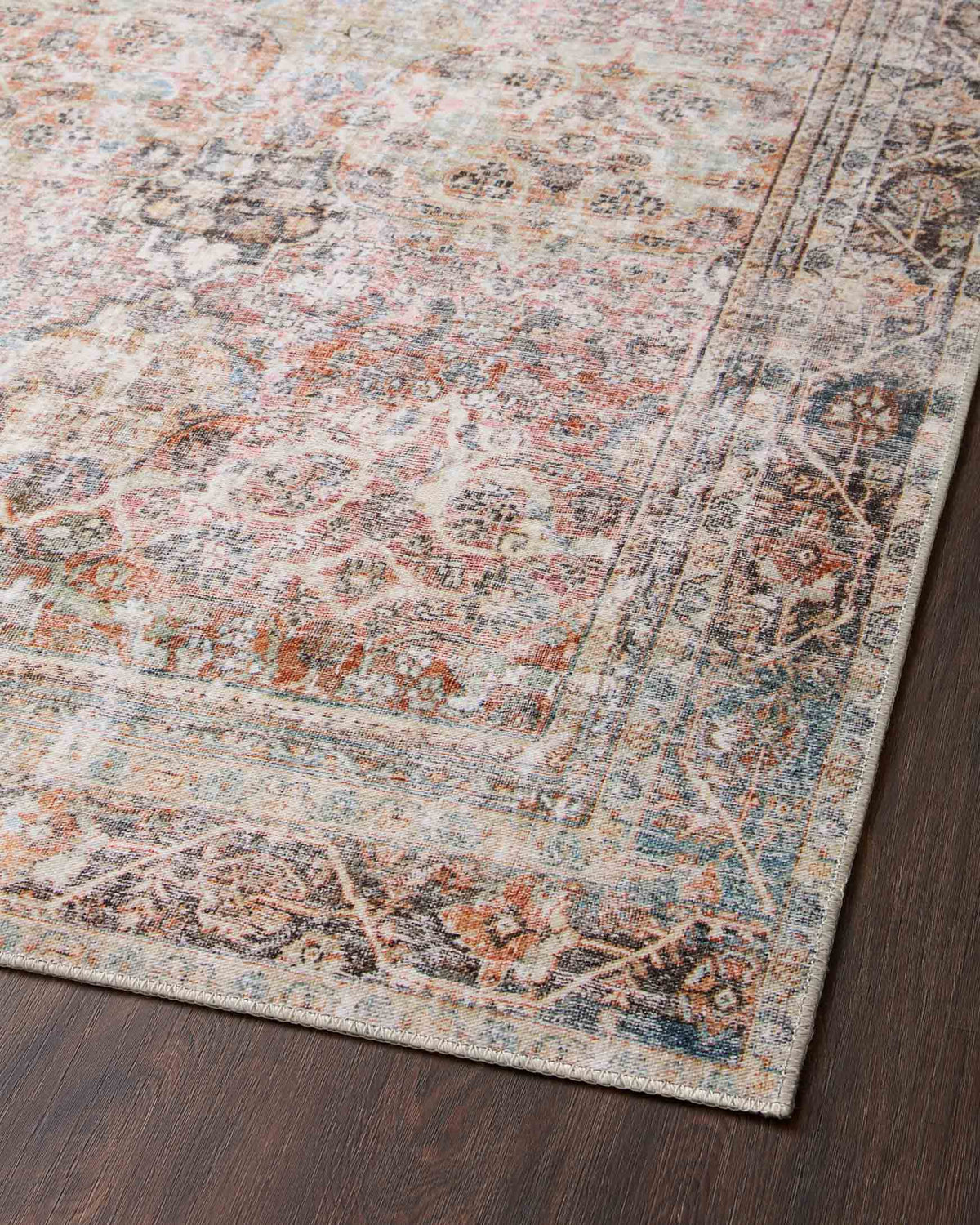 Traditional power-loomed rug close-up with distressed corner motif and border in rust and teal.