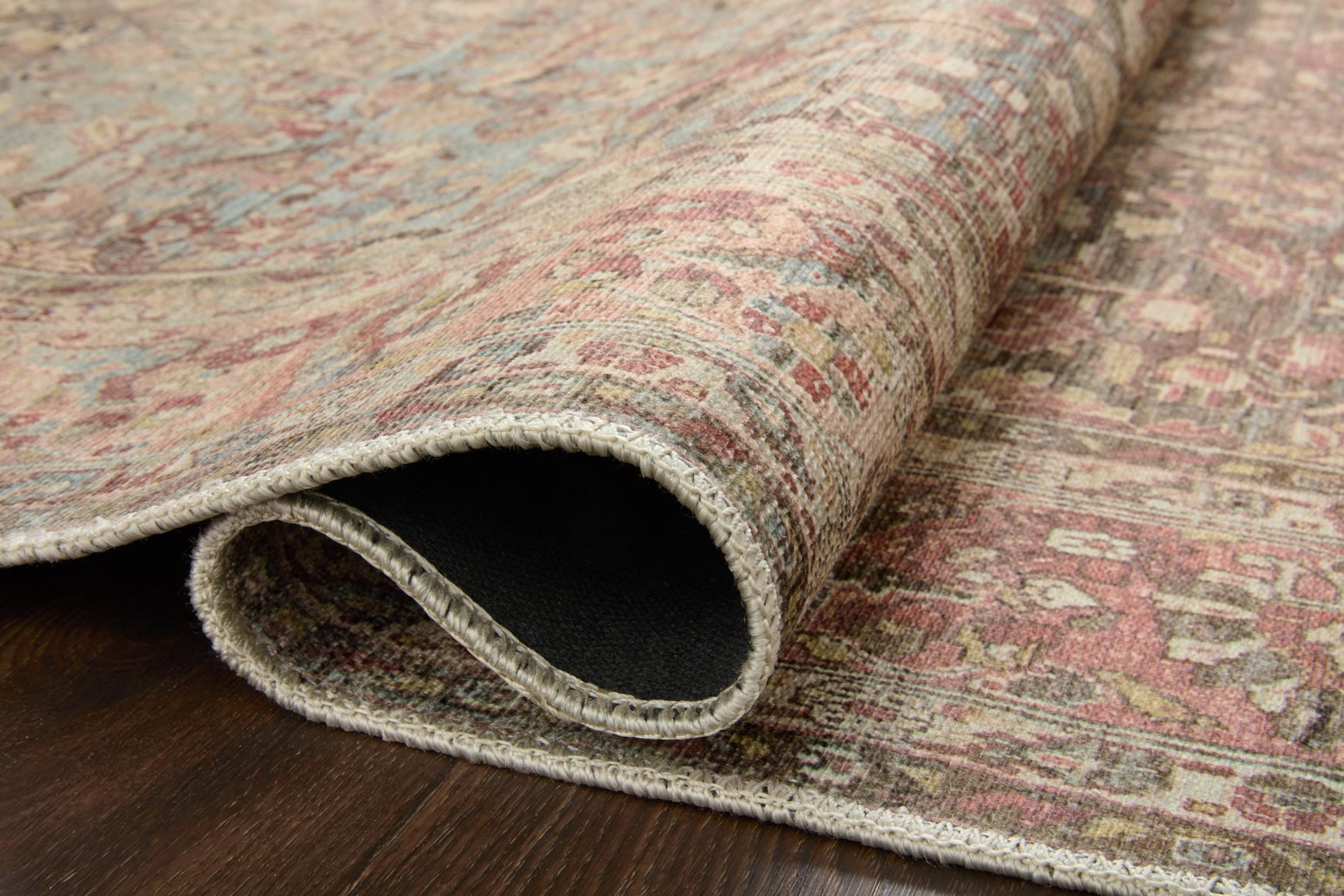 Rolled edge of ornate area rug, showing low pile and multicolor woven border.