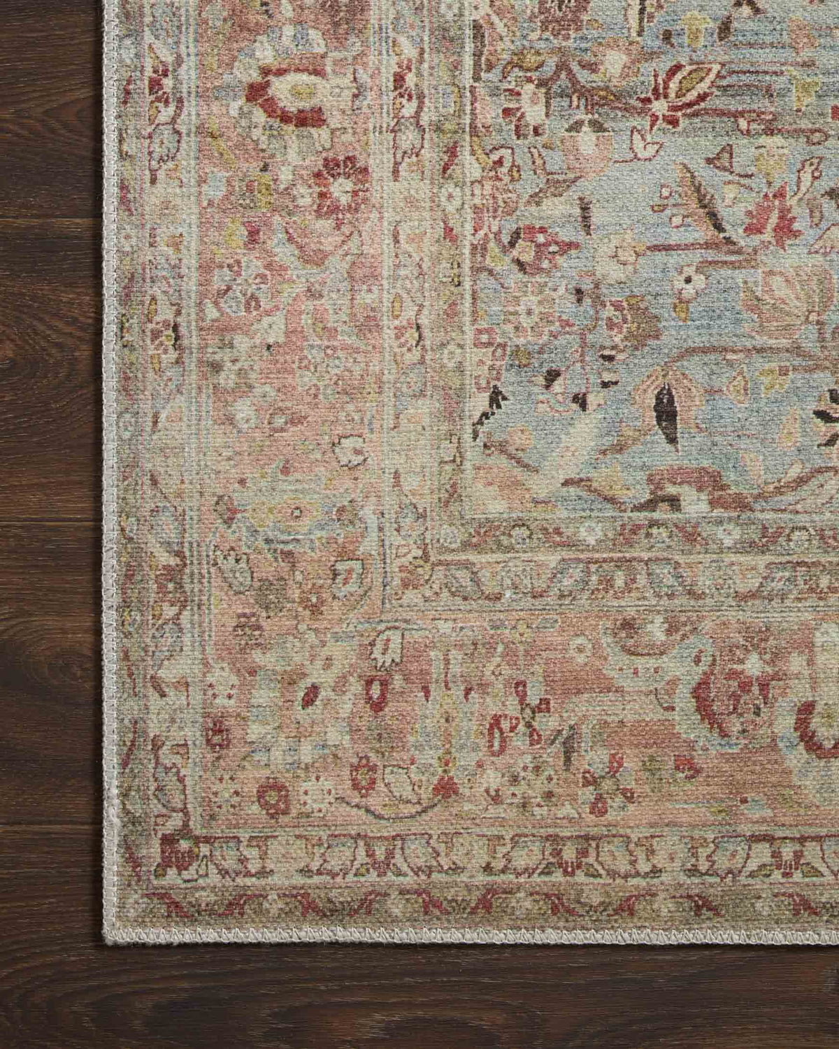 Close-up of ornate rug pattern with blue, red, and tan motifs and detailed trim.