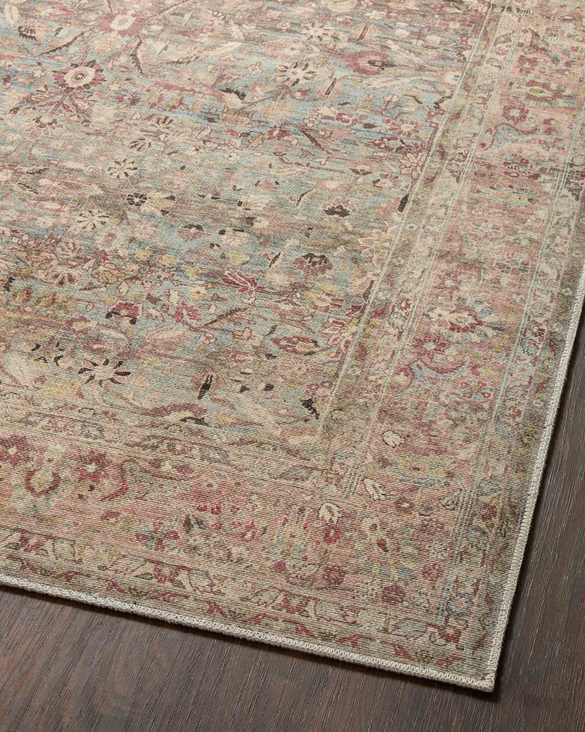 Close-up overhead view of ornate area rug with scattered motifs in ocean blue and clay pink.