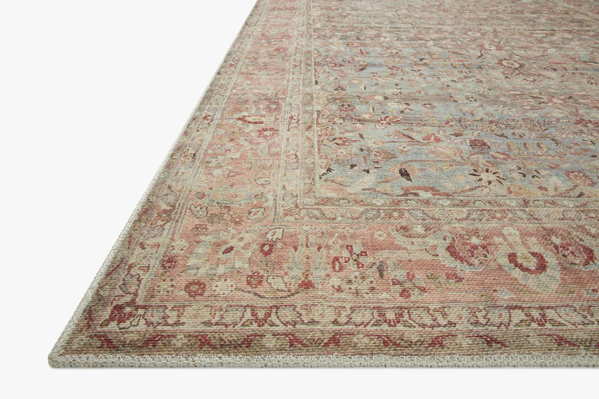 Angled close-up of ornate area rug corner with muted blue, pink, and tan details.