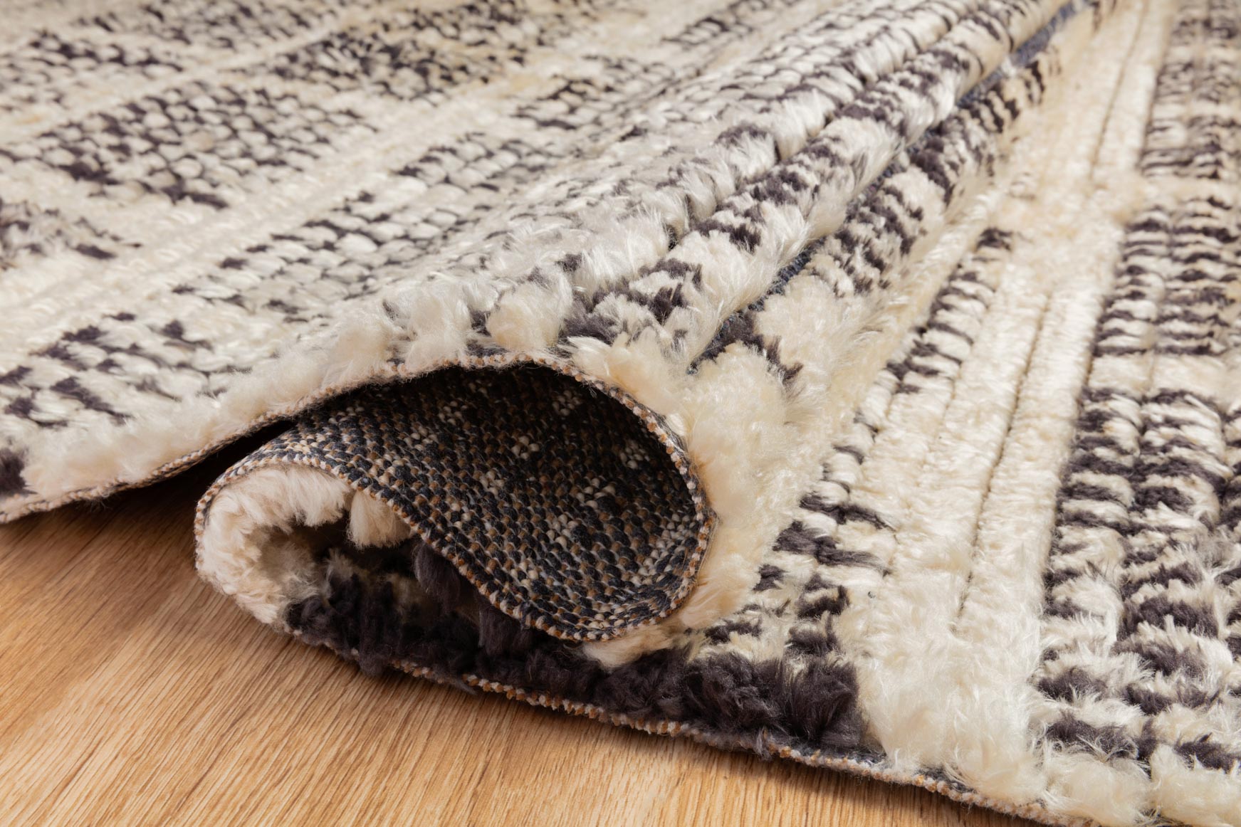 Cream and charcoal rug folded corner showing underside pile and stitched edge detail