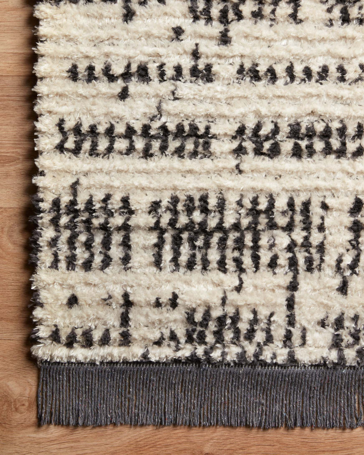 Cream and charcoal rug close-up with grid motif and dark fringe border on the edge