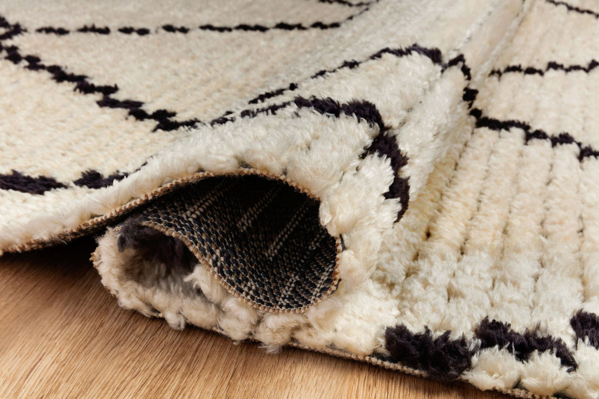 Close-up of cream rug with charcoal lines and textured pile, rolled corner detail.