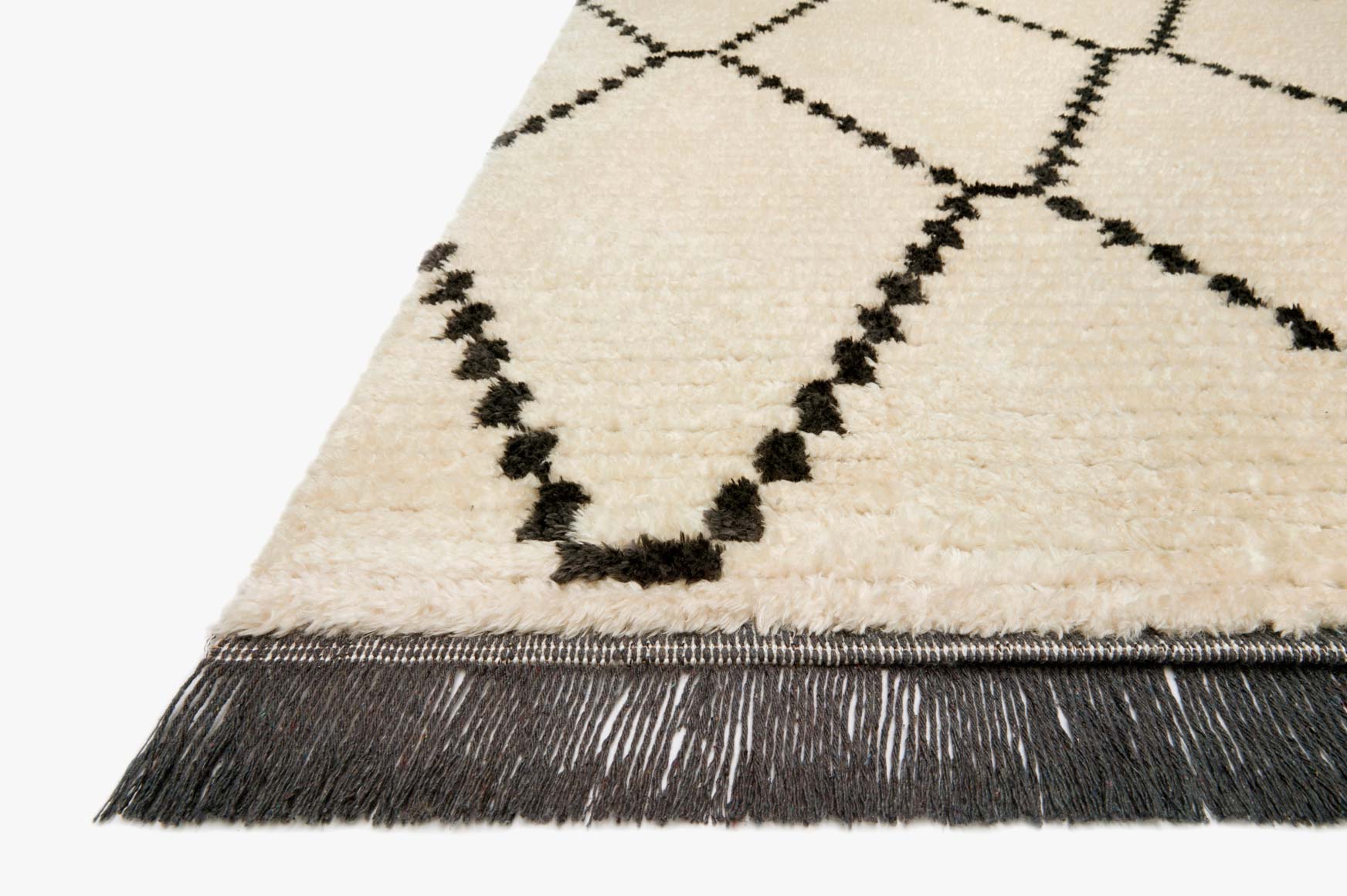 Corner view of cream rug with charcoal diamonds and dark fringe along the edge.