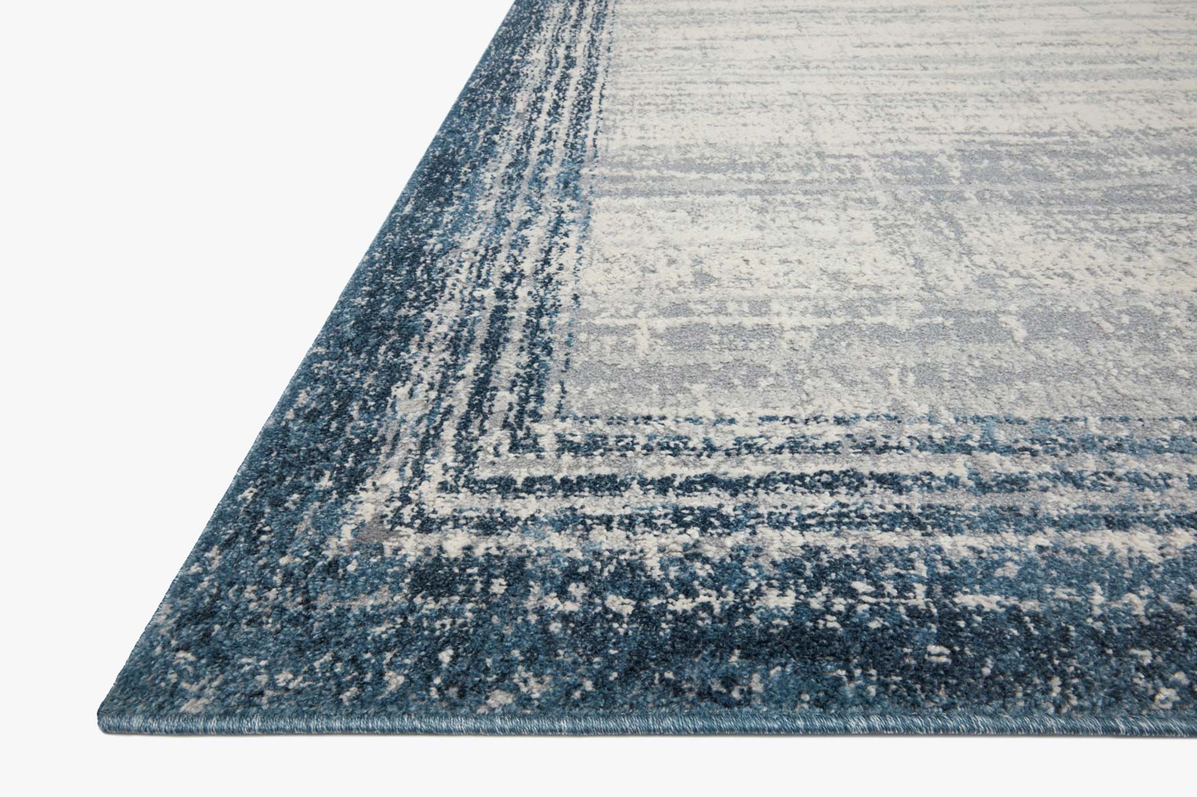 Pebble-and-blue rug corner view with distressed border lines and textured weave