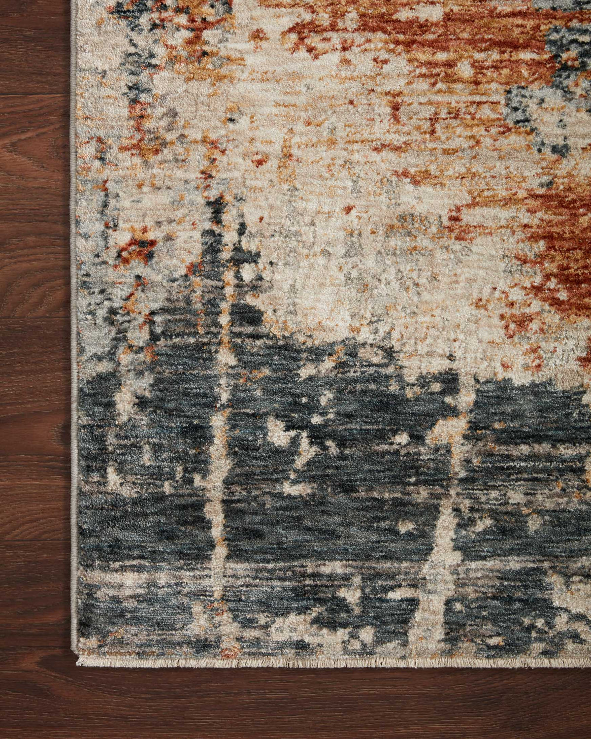 Close-up of power-loomed rug edge showing stone base with rust and dark blue-gray pattern.