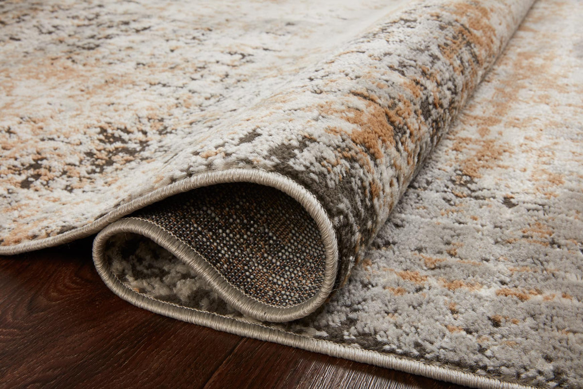 Rolled edge detail of stone and gold abstract rug with dark speckled pile