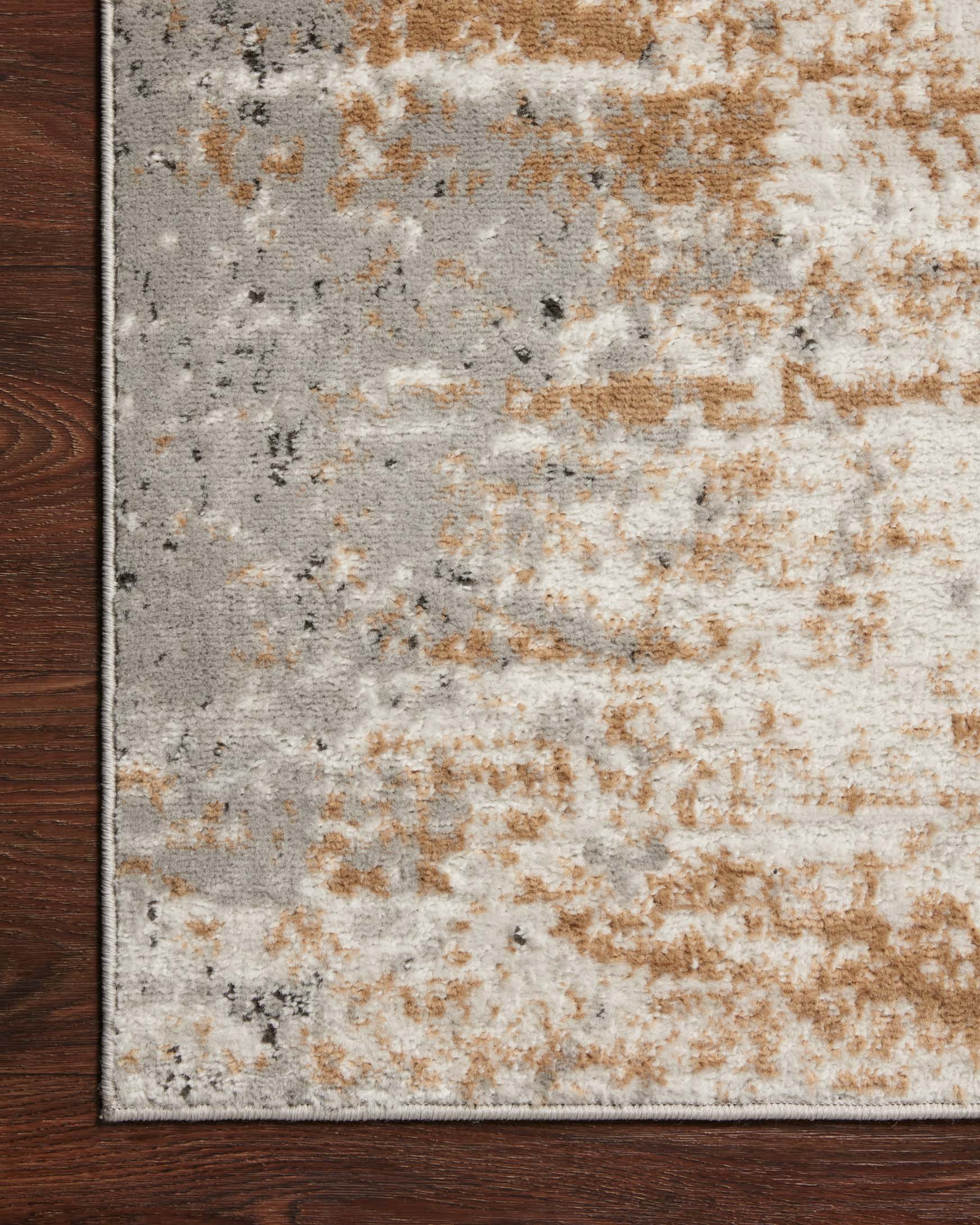 Corner close-up of stone and gold abstract area rug with distressed texture and flecks
