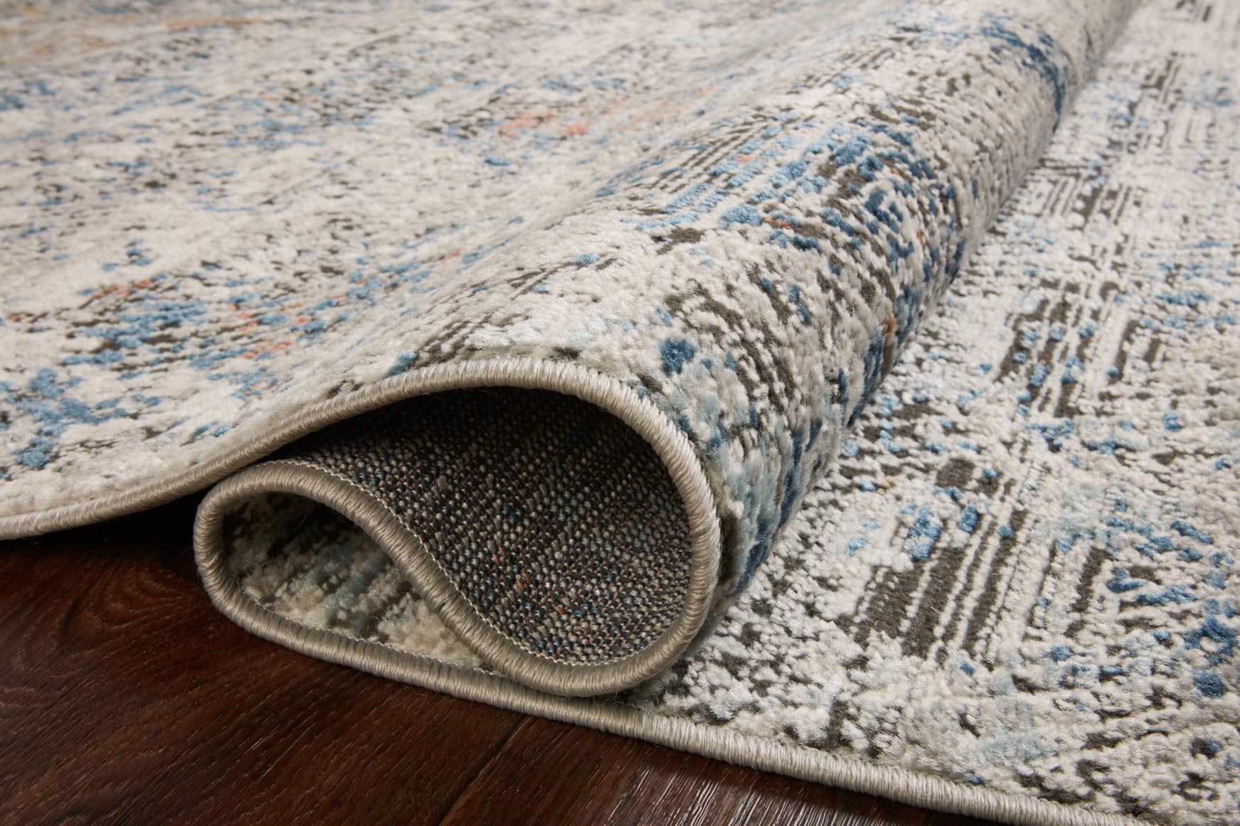 Rolled edge of grey abstract rug showing short pile and stitched border, blue accents