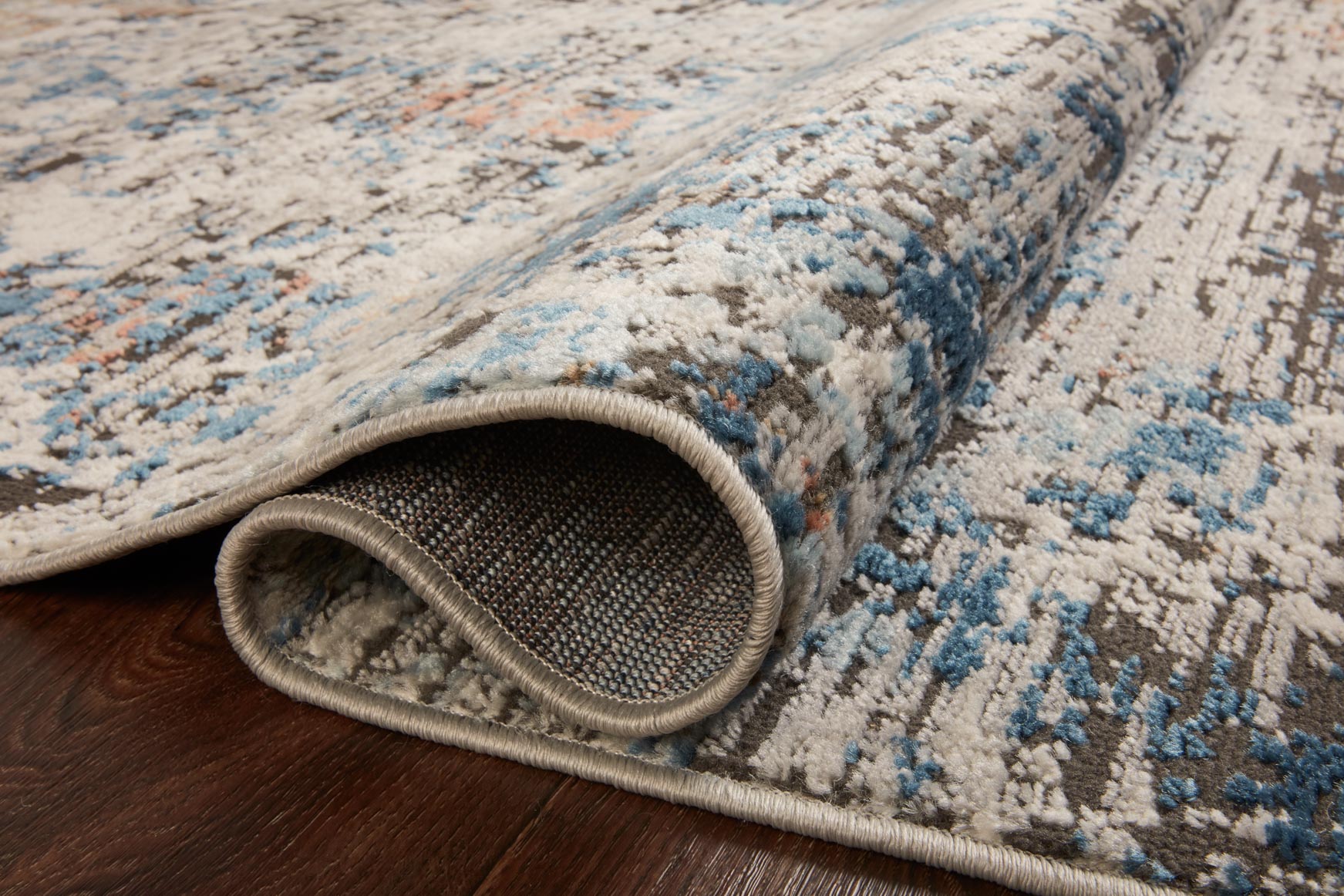 Textured area rug surface with gray pile and blue and rust flecks, bound edge.
