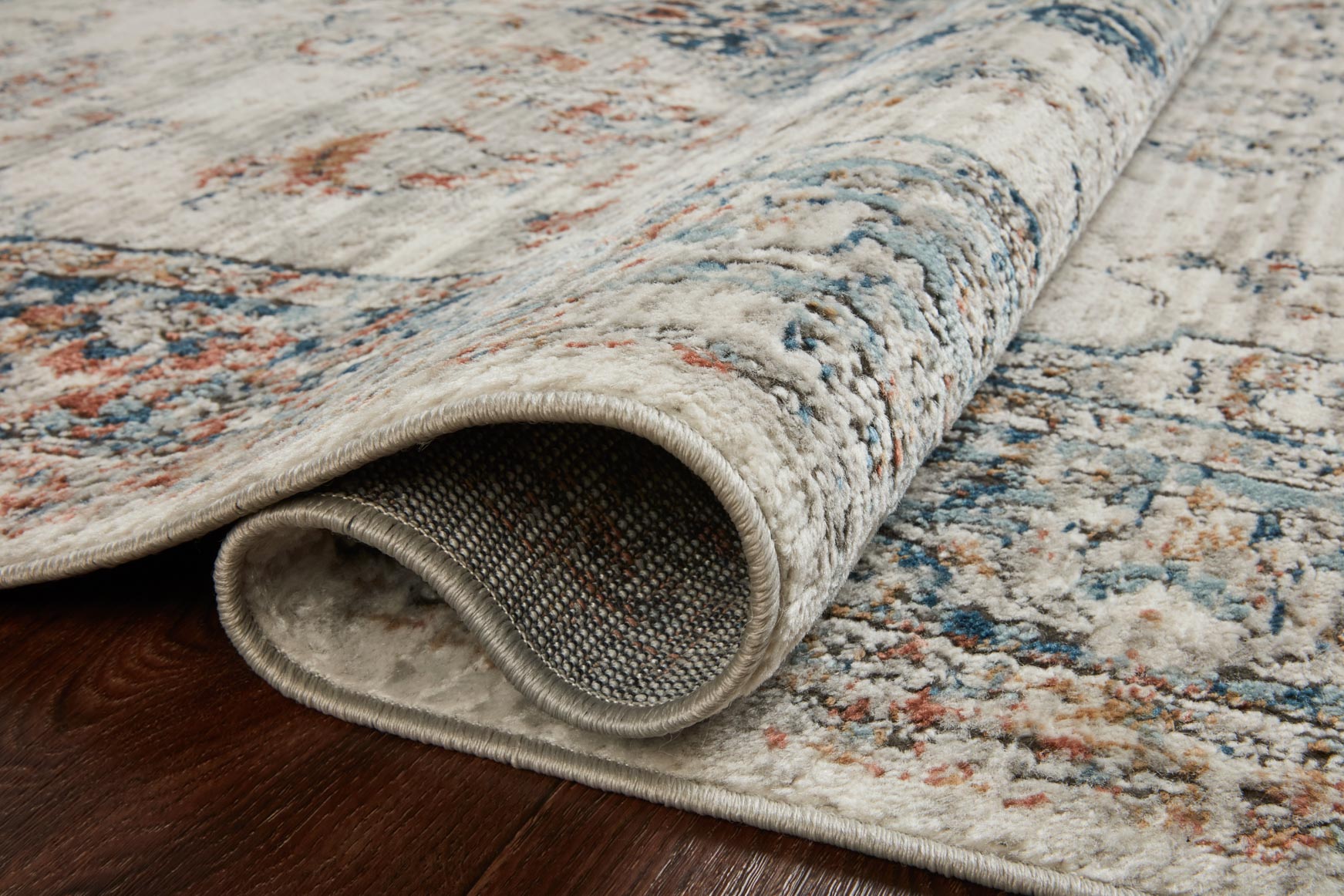 Folded edge of ivory rug, blue and orange distressed pattern, textured pile underside