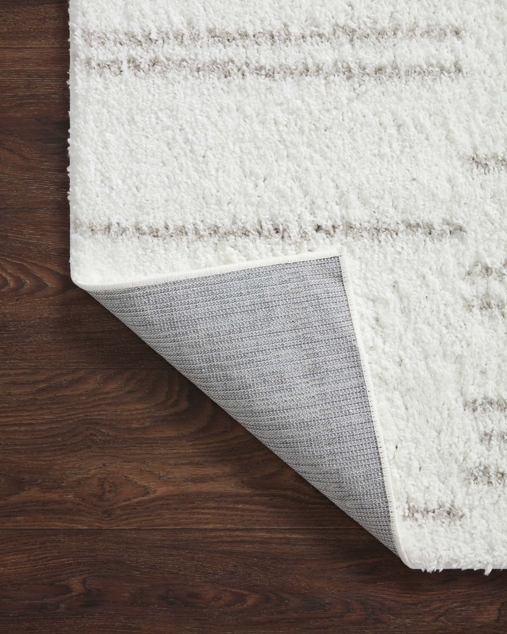 White shag rug with rolled edge showing grey woven backing and stitching